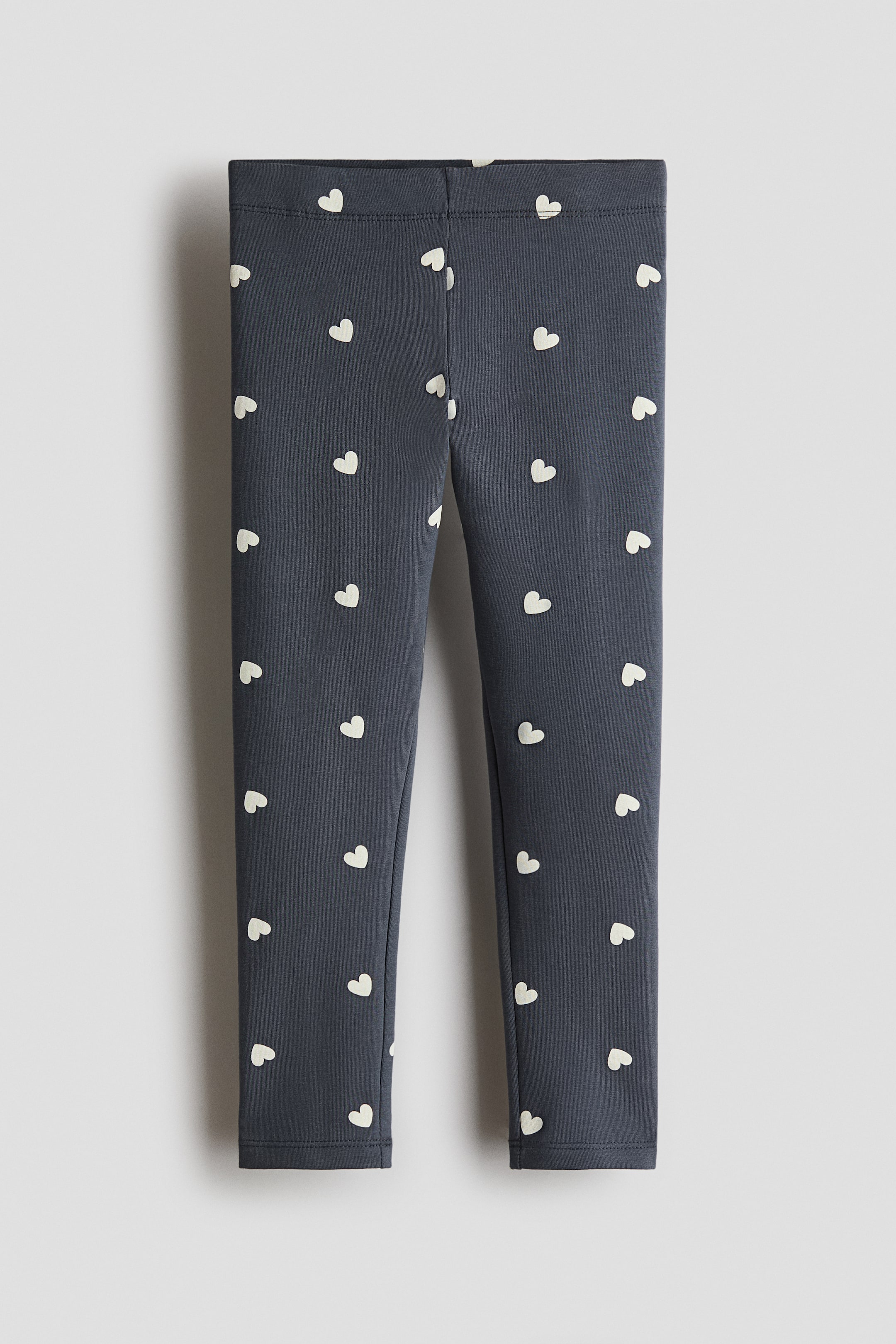 View larger image: Dark grey leggings feature a repeating pattern of small, light-coloured heart shapes across the front, with an elasticated waistband forming the top edge.