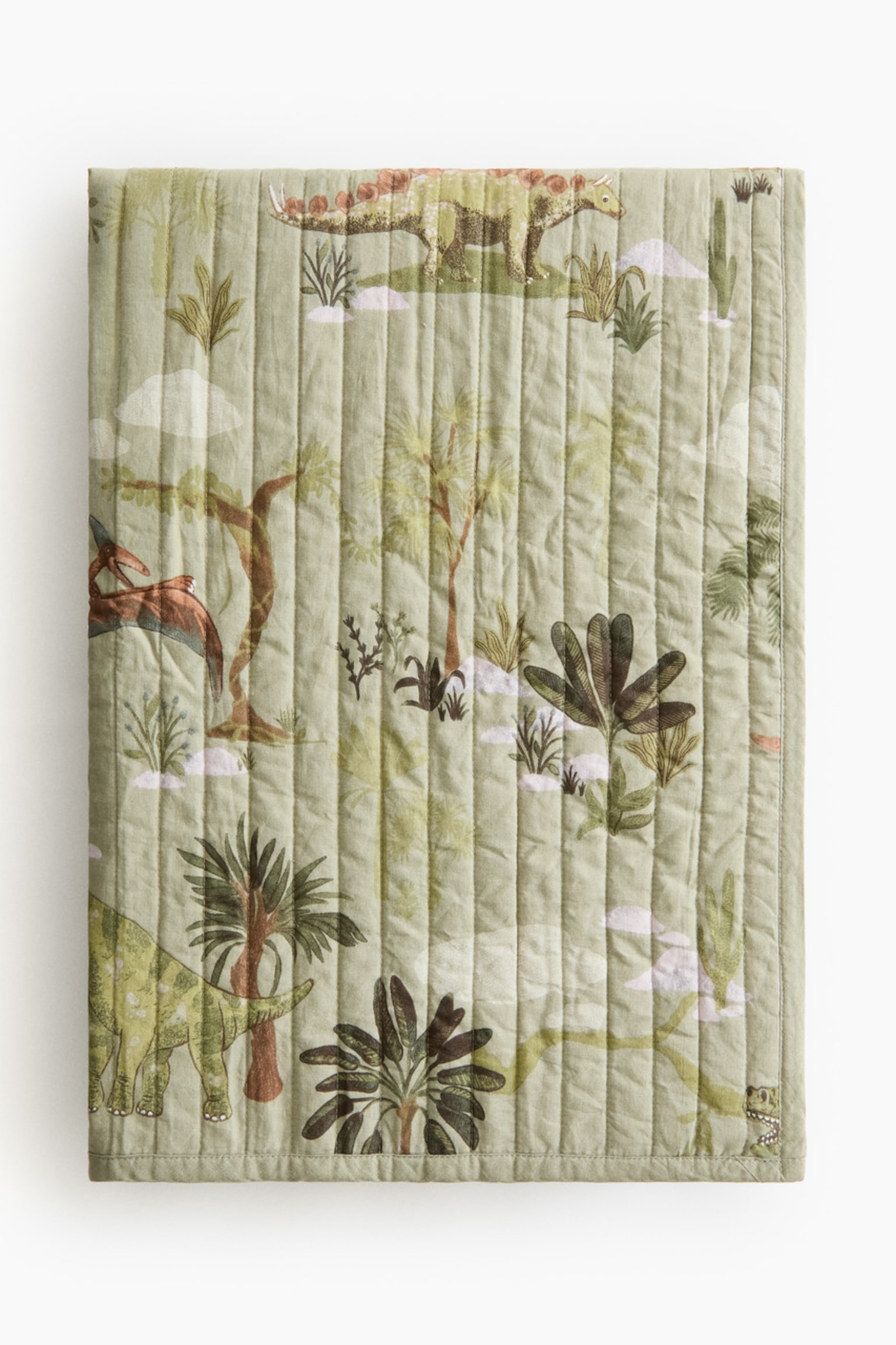A light green quilted blanket showcases a pattern of dinosaurs, including a Stegosaurus and Pterodactyl, amidst various trees and plants. It features vertical quilting stitches across its entire front surface. - 1