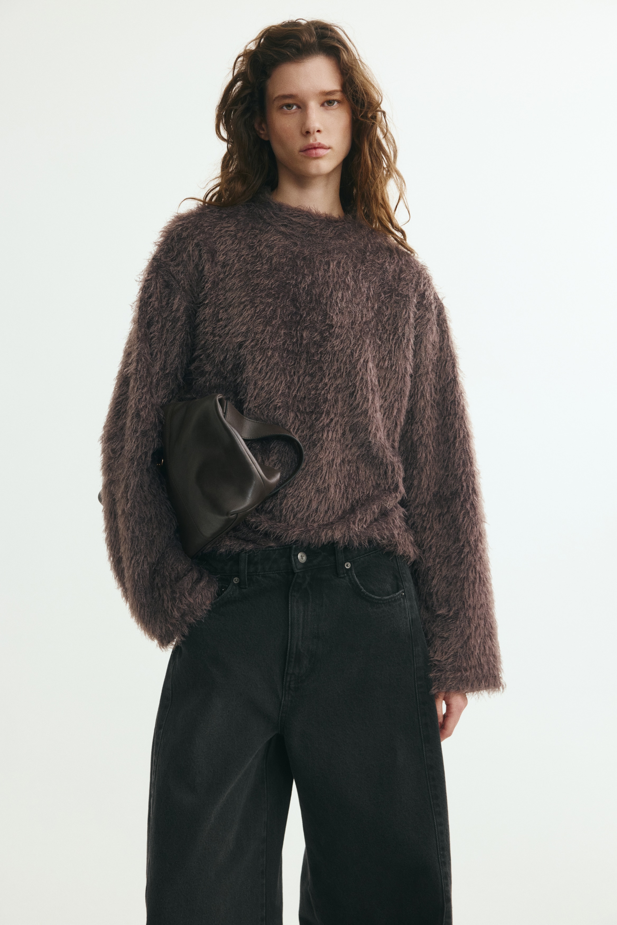 A dark grey shaggy knit sweater is hanging front-facing, featuring a mock neck, long wide sleeves, and an all-over fluffy, long-haired texture.