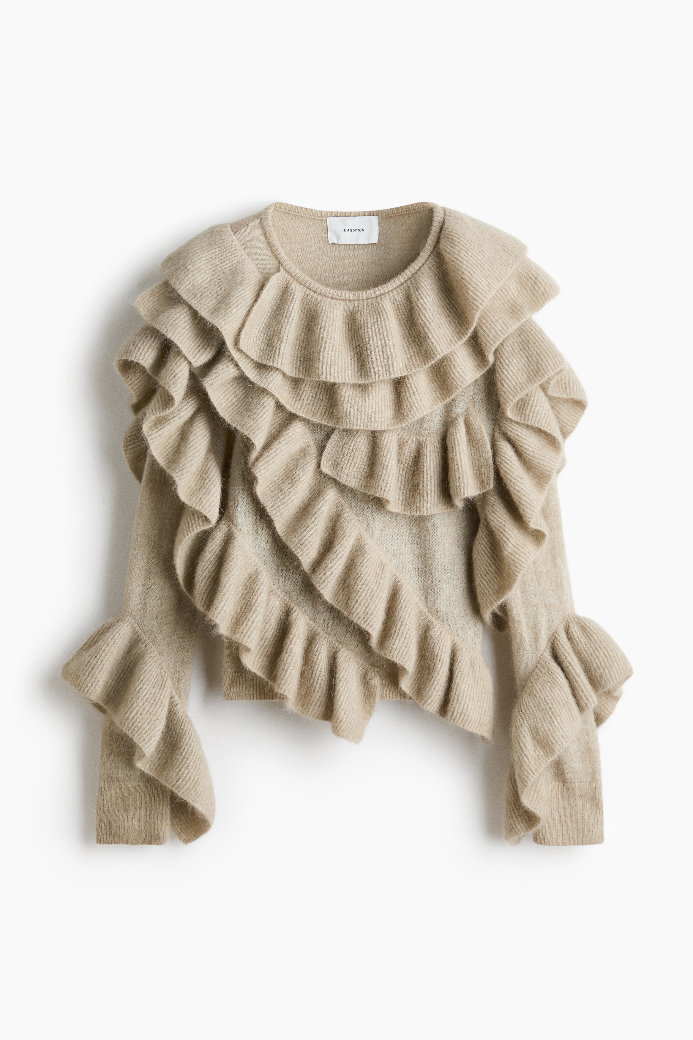Un pull en maille beige, ornÃ© de volants Ã  cÃ´tes superposÃ©s sur lâensemble du devant et des manches, est portÃ© par le mannequin. Le pull prÃ©sente un col rond, des Ã©paules tombantes et des manches longues avec des poignets volantÃ©s Ã©vasÃ©s, ici associÃ© Ã  un pantalon noir.