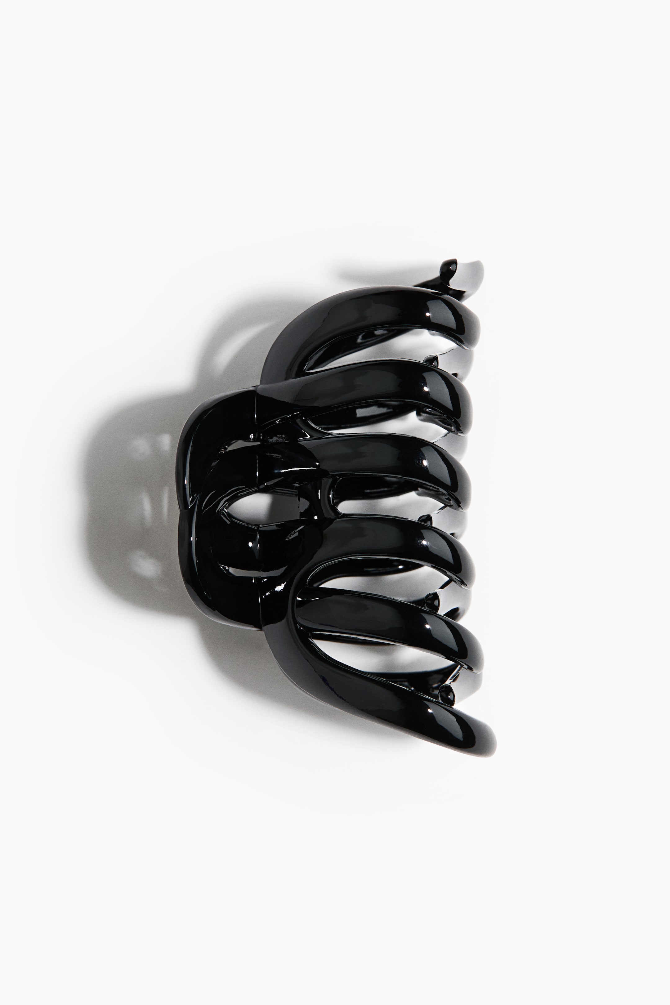 Größeres Bild ansehen: Haarklammer aus Kunststoff. Eine glänzend schwarze Haarklammer ist frontal ausgerichtet und präsentiert ein gewundenes, spiralförmiges Design mit mehreren ineinandergreifenden Segmenten.