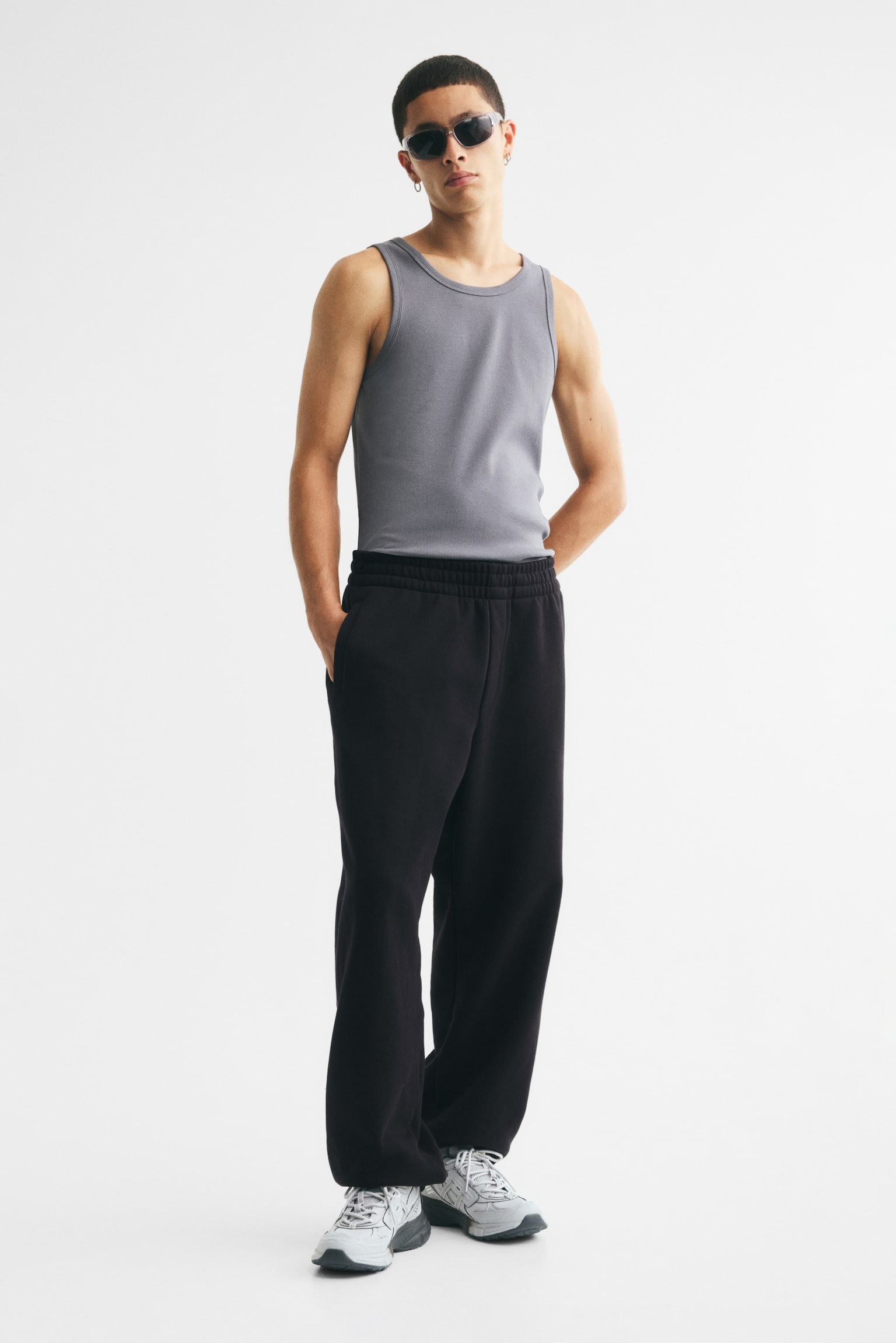 Black sweatpants are presented from the front, featuring an elasticated waistband and two vertical side pockets. The legs taper down to elasticated cuffs at the ankles. - 1