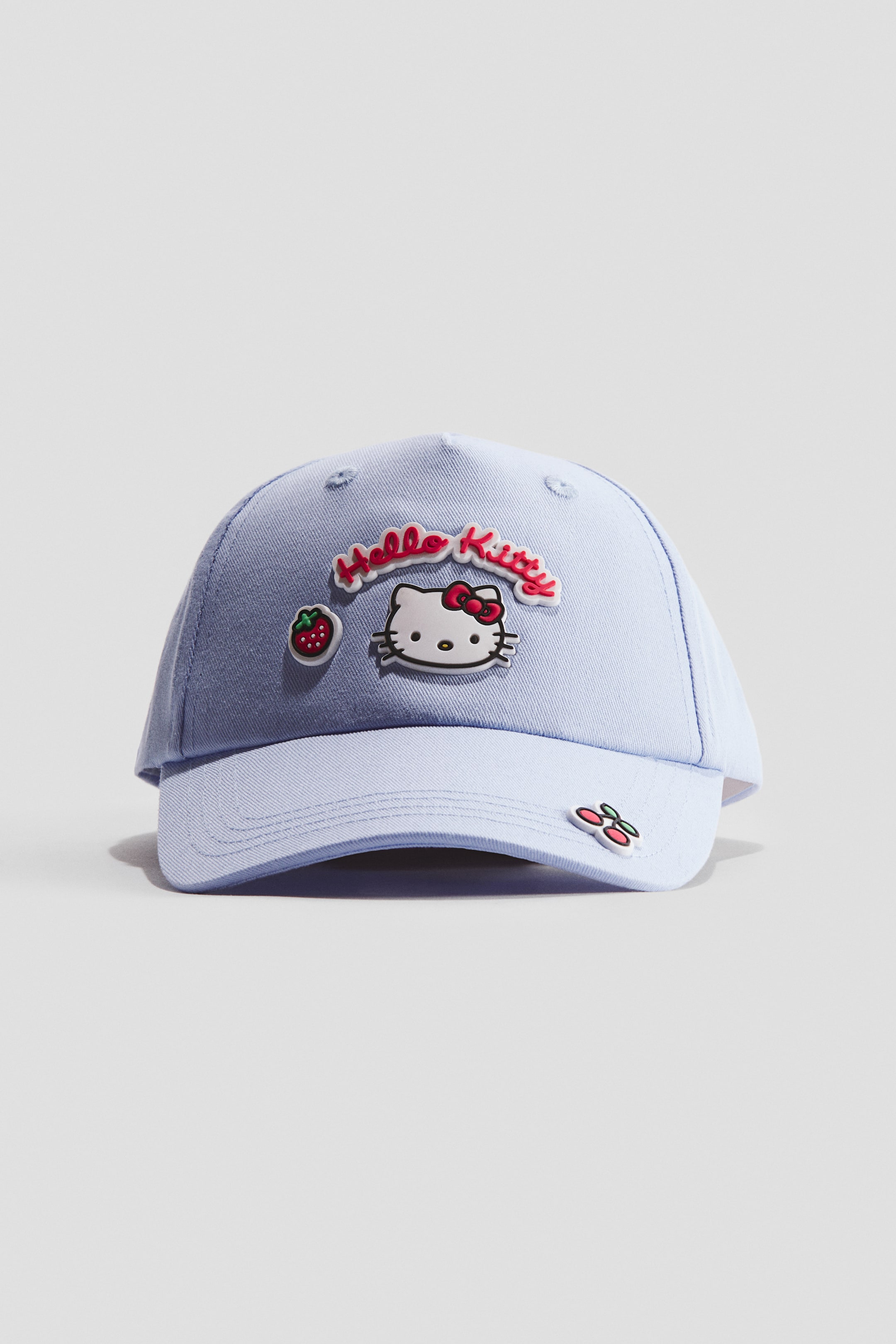 Zobacz większy obraz: Jasnoniebieska czapka z bawełnianego diagonalnego splotu jest skierowana do przodu, prezentując szczegóły motywu, w tym napis "Hello Kitty", twarz Hello Kitty oraz truskawkę na przednim panelu, z widoczną wiśnią na daszku. Na koronie znajdują się również haftowane otwory.