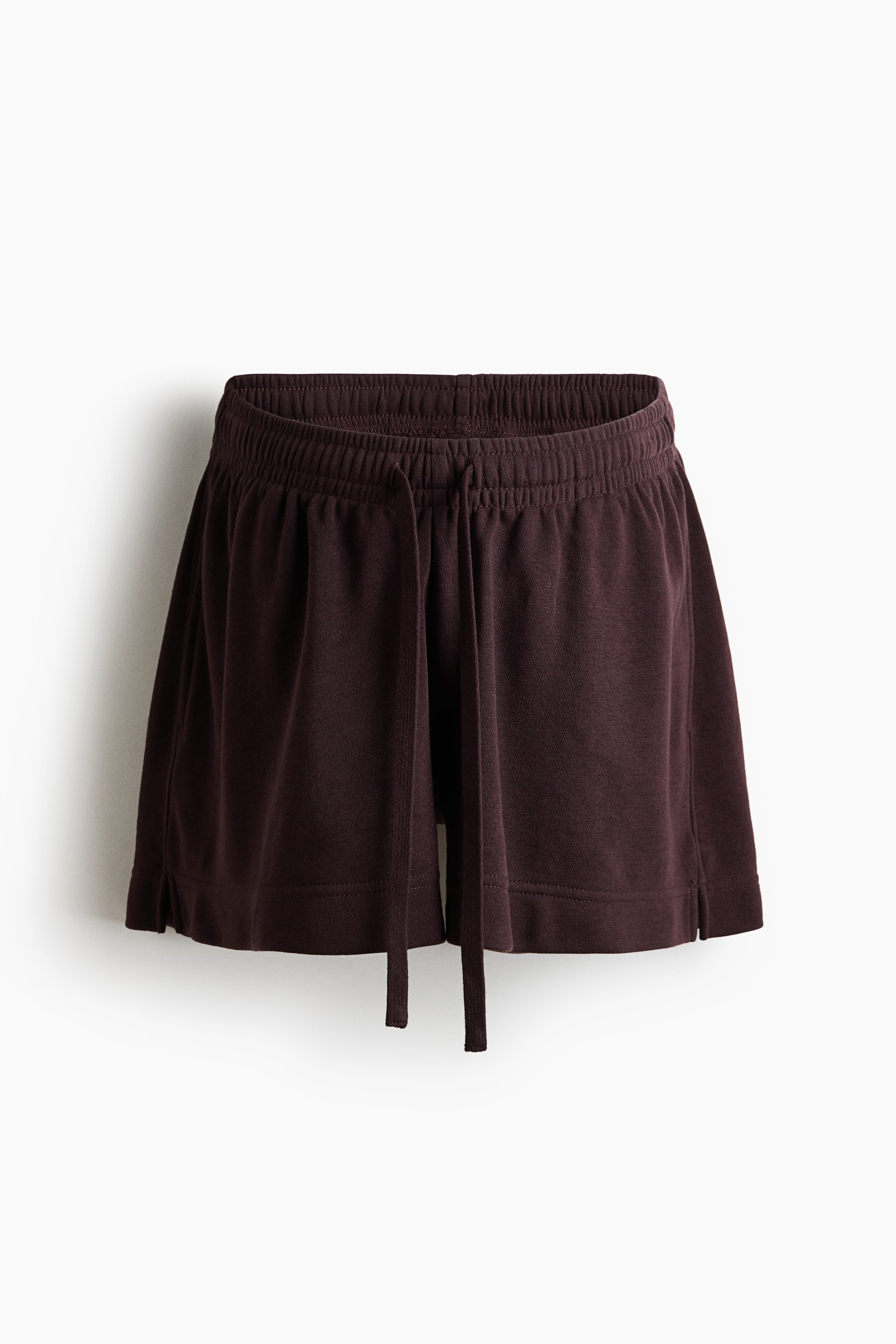 Größeres Bild anzeigen: Dunkelbraune Shorts werden von vorne präsentiert, mit einem elastischen, gerafften Bund und einem flachen, stoffeigenen Kordelzug, der vorne herunterhängt. Die Shorts zeigen ein weit geschnittenes Design mit kleinen seitlichen Schlitzen am Saum.