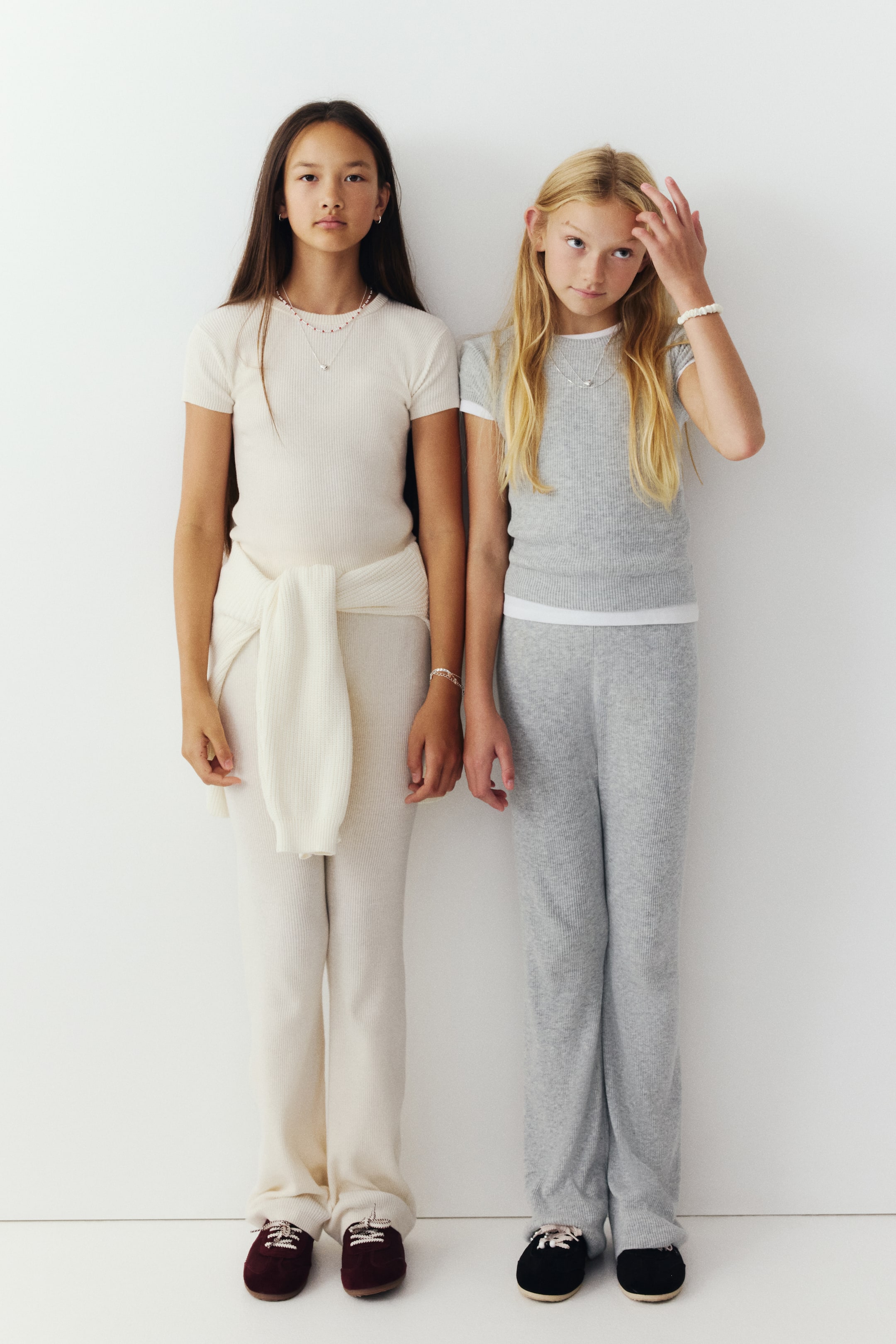 Grösseres Bild ansehen: Zwei zweiteilige Sets aus gerippter Baumwollmischung mit Oberteil und Hose werden von vorne in Creme und Hellgrau gezeigt. Jedes Set besteht aus einem kurzärmeligen Top mit Rundhalsausschnitt und einer passenden Wide-Leg-Hose, wobei das cremefarbene Set mit einem passenden Pullover um die Taille gebunden gestylt ist.