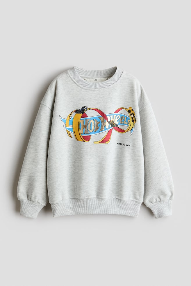 En ljusgrÃ¥ melerad sweatshirt i loose fit visas framifrÃ¥n, med ett fÃ¤rgstarkt Hot Wheels-tryck pÃ¥ brÃ¶stet och texten "RACE TO WIN" tryckt nedanfÃ¶r. Plagget Ã¤r designat med en rund halsringning med ribbad kant, nedhasade axlar och lÃ¥nga Ã¤rmar som avslutas med ribbade muddar, i matchande ribbad nederkant. - 1