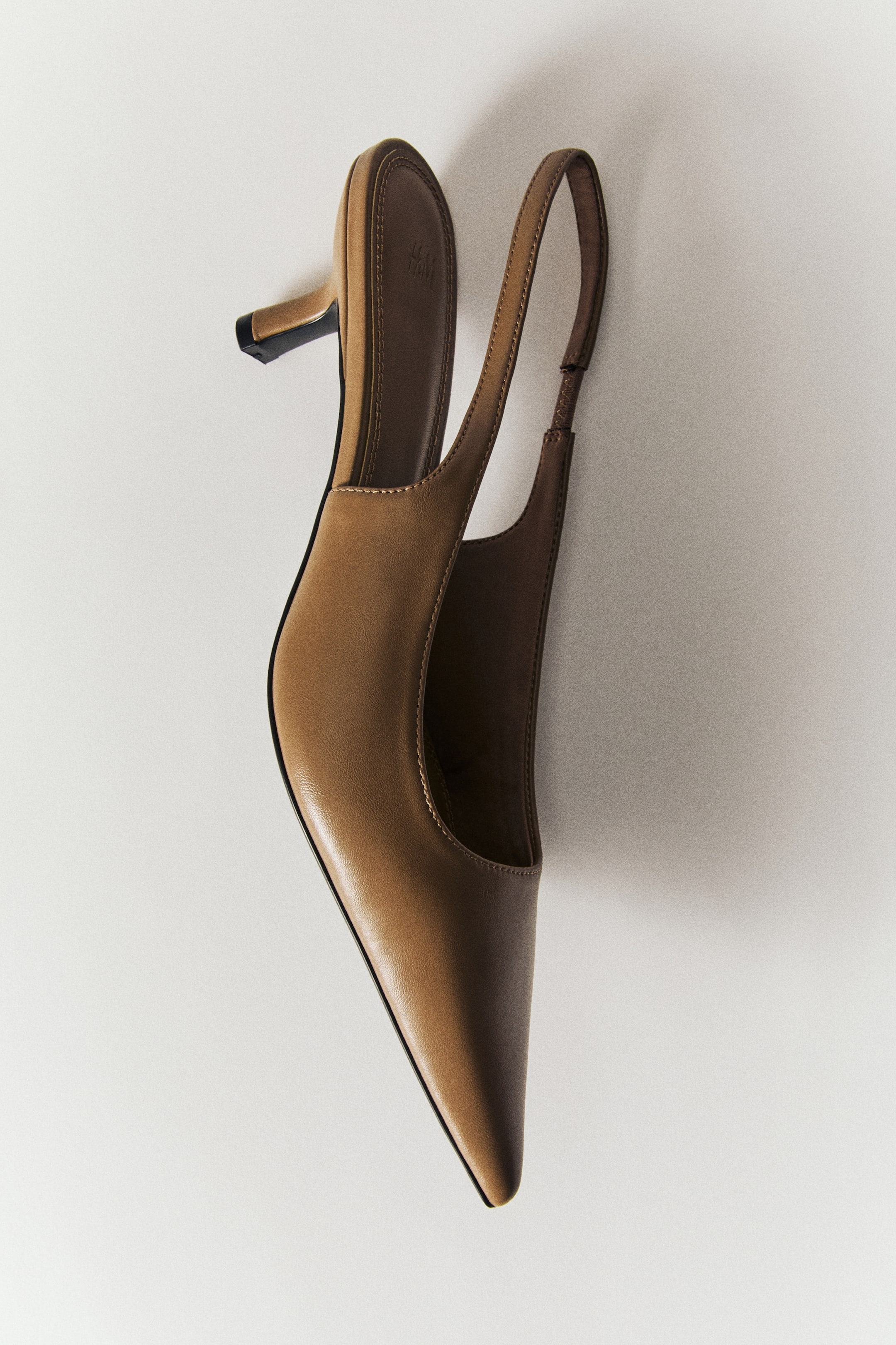View larger image: Slingback court shoe in light brown featuring a pointed toe, a narrow heel strap with a small elasticated insert, and a low kitten heel. The shoe is positioned on its side to display its smooth matte finish, inner sole lining, and sleek silhouette.