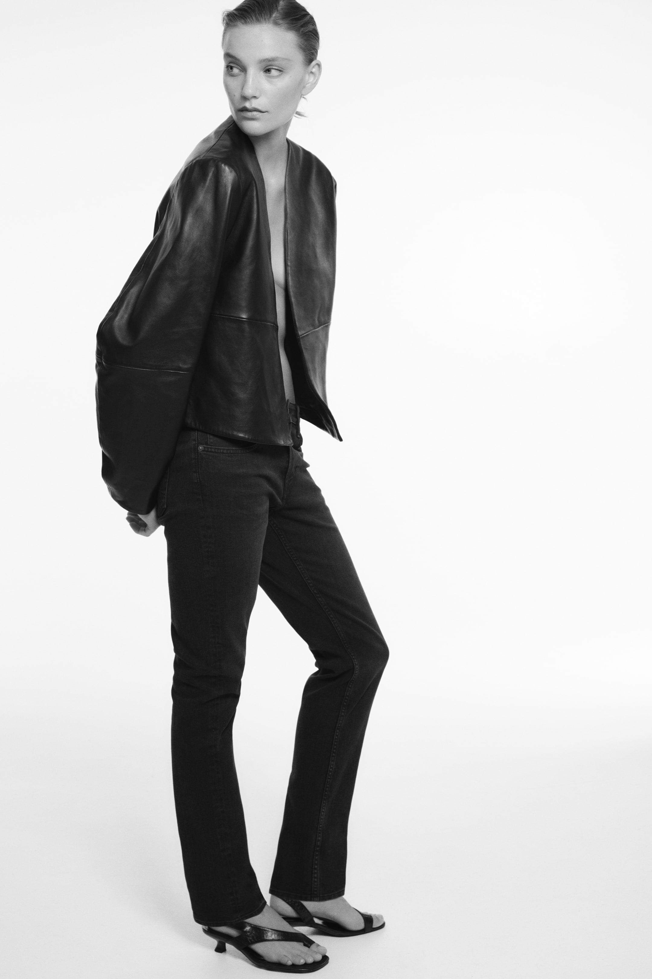 Grotere afbeelding bekijken: De donkerblauwe five-pocket jeans in denim worden getoond vanuit een driekwart zijaanzicht, met een slim fit rond de taille en dijen en een versmallende skinny pasvorm bij de enkels met weinig stacking. De jeans worden gecombineerd met een zwarte leren jas en sandalen met hak, waardoor de normale taille en het gestructureerde silhouet worden benadrukt.