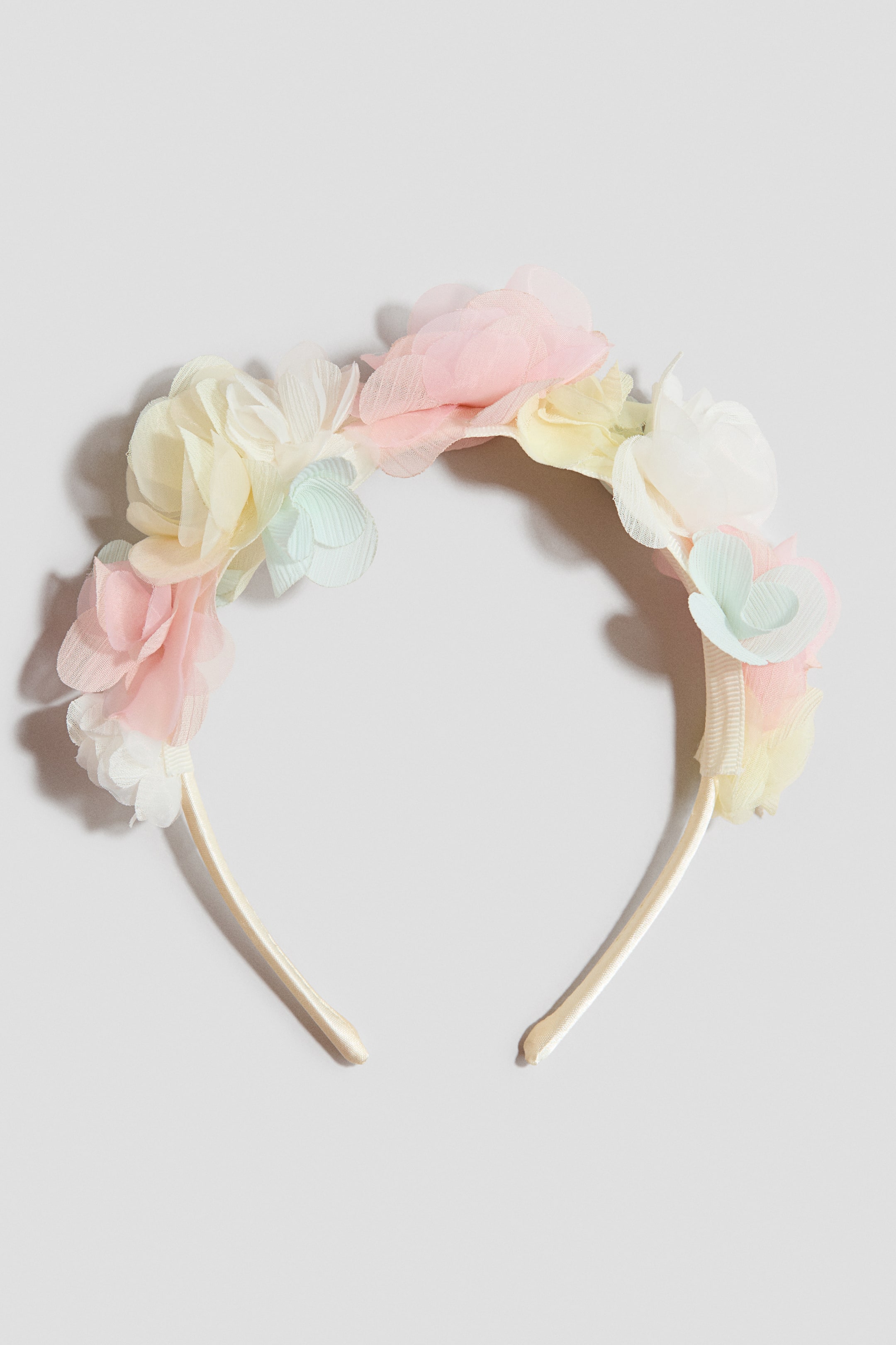 View larger image: The headband showcases an arrangement of pastel fabric flowers at the front. The layered blooms appear in shades of pink, yellow, light blue, and white, clustered along the top of the cream-colored band.