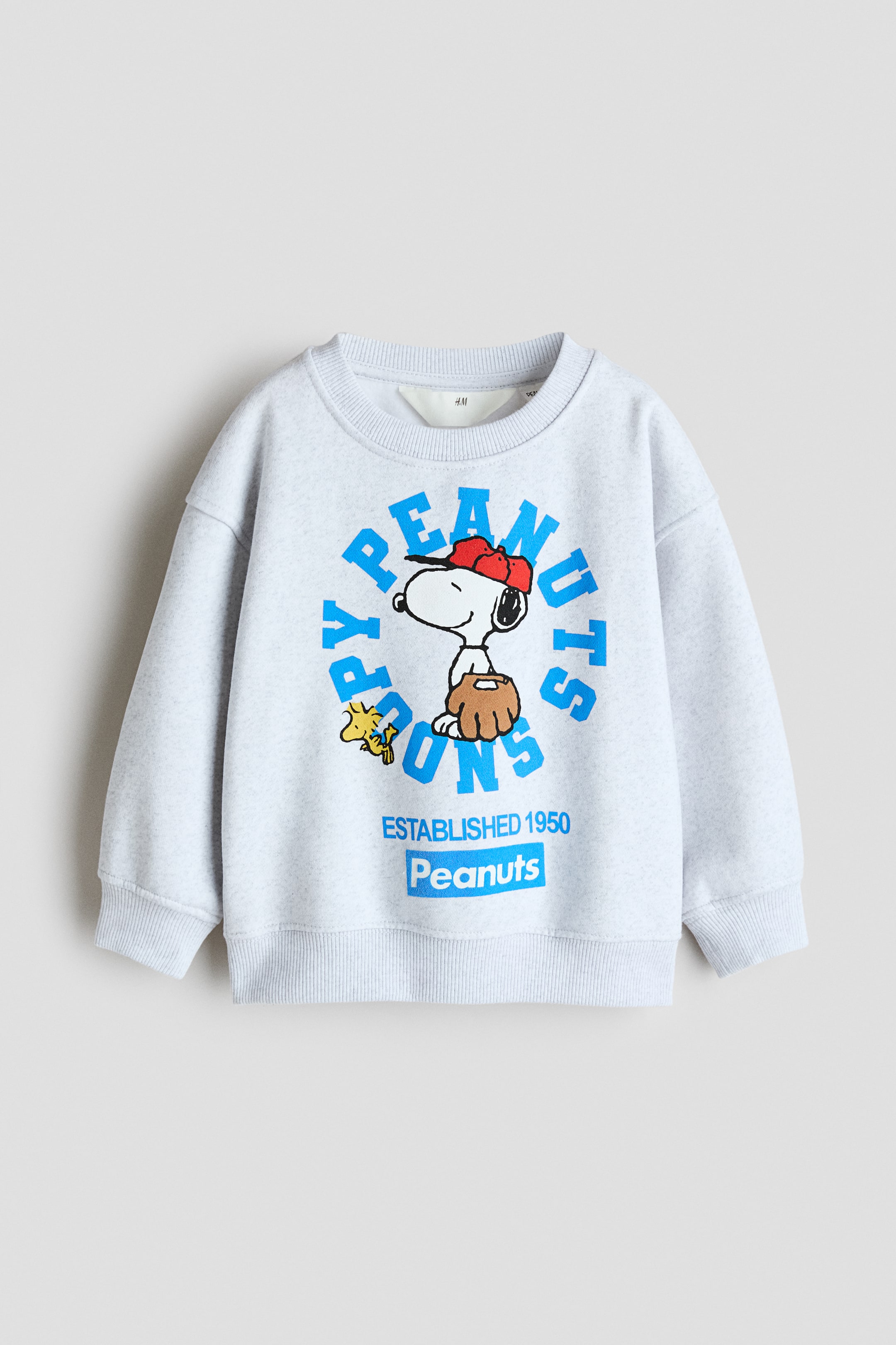View larger image: A light grey melange sweatshirt is shown from the front, featuring a round, rib-trimmed neckline, dropped shoulders, and ribbed cuffs and hem. The front displays a printed graphic of Snoopy wearing a red cap and holding a baseball glove, surrounded by arched blue text, with additional branding text printed below.