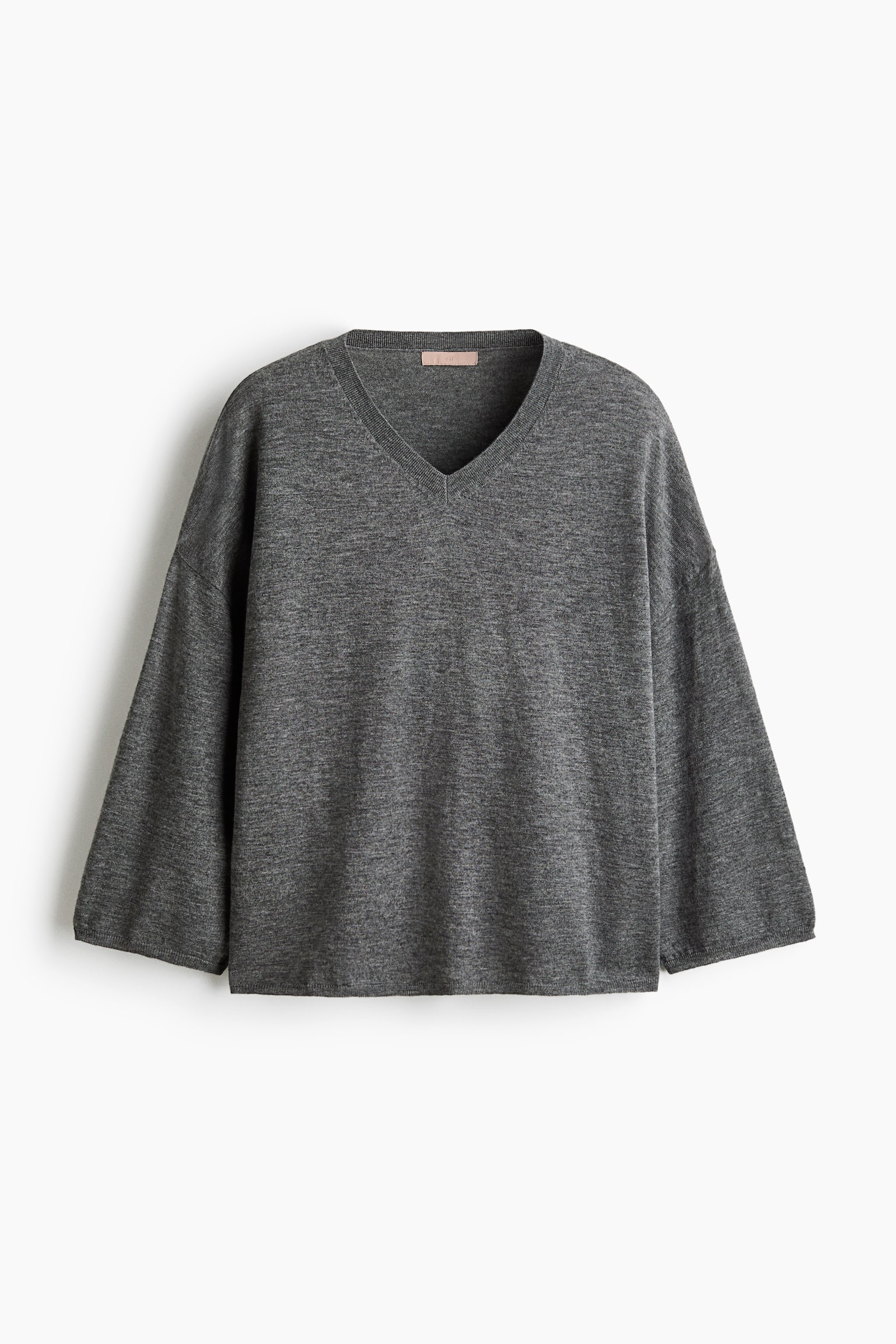 A heather grey knit jumper is shown from the front, featuring a relaxed fit with dropped shoulders and wide, slightly flared sleeves. The jumper features a ribbed V-neckline and a clean, straight hem.