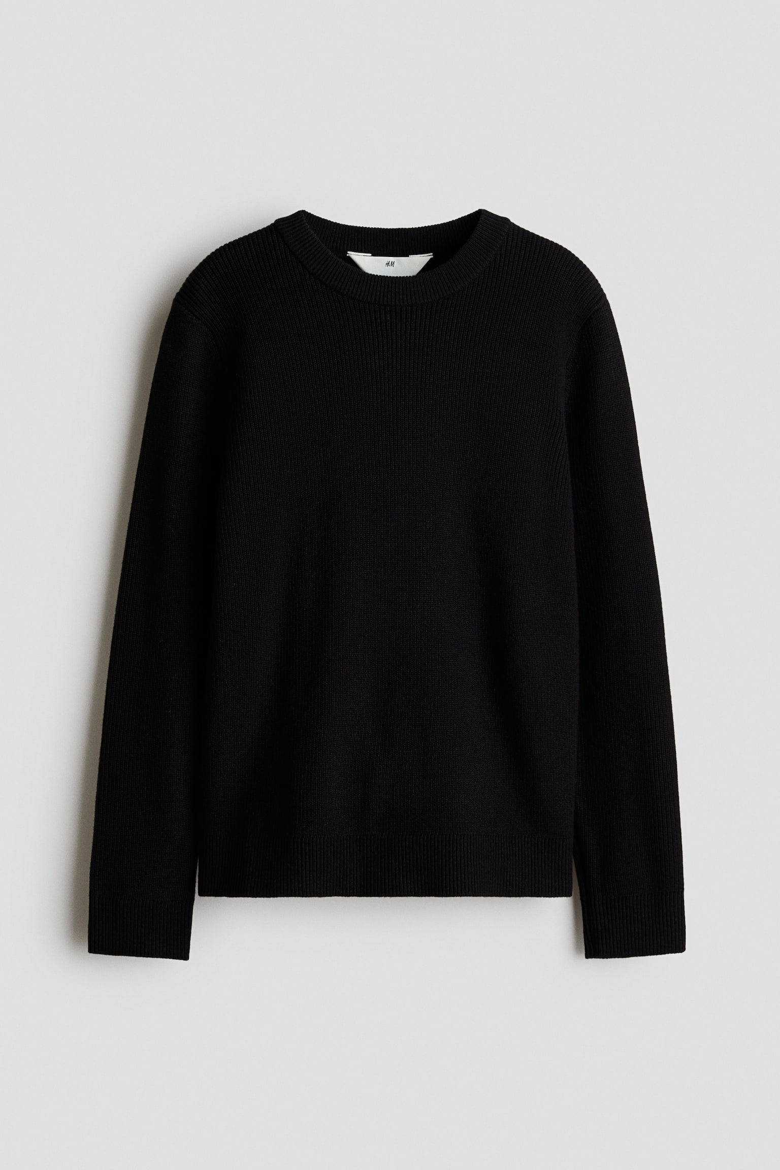 Frontvisning af en sort sweater i blÃ¸d ribstrik med rund halsudskÃ¦ring med ribkant, lange Ã¦rmer med ribmanchetter og ribkant forneden.