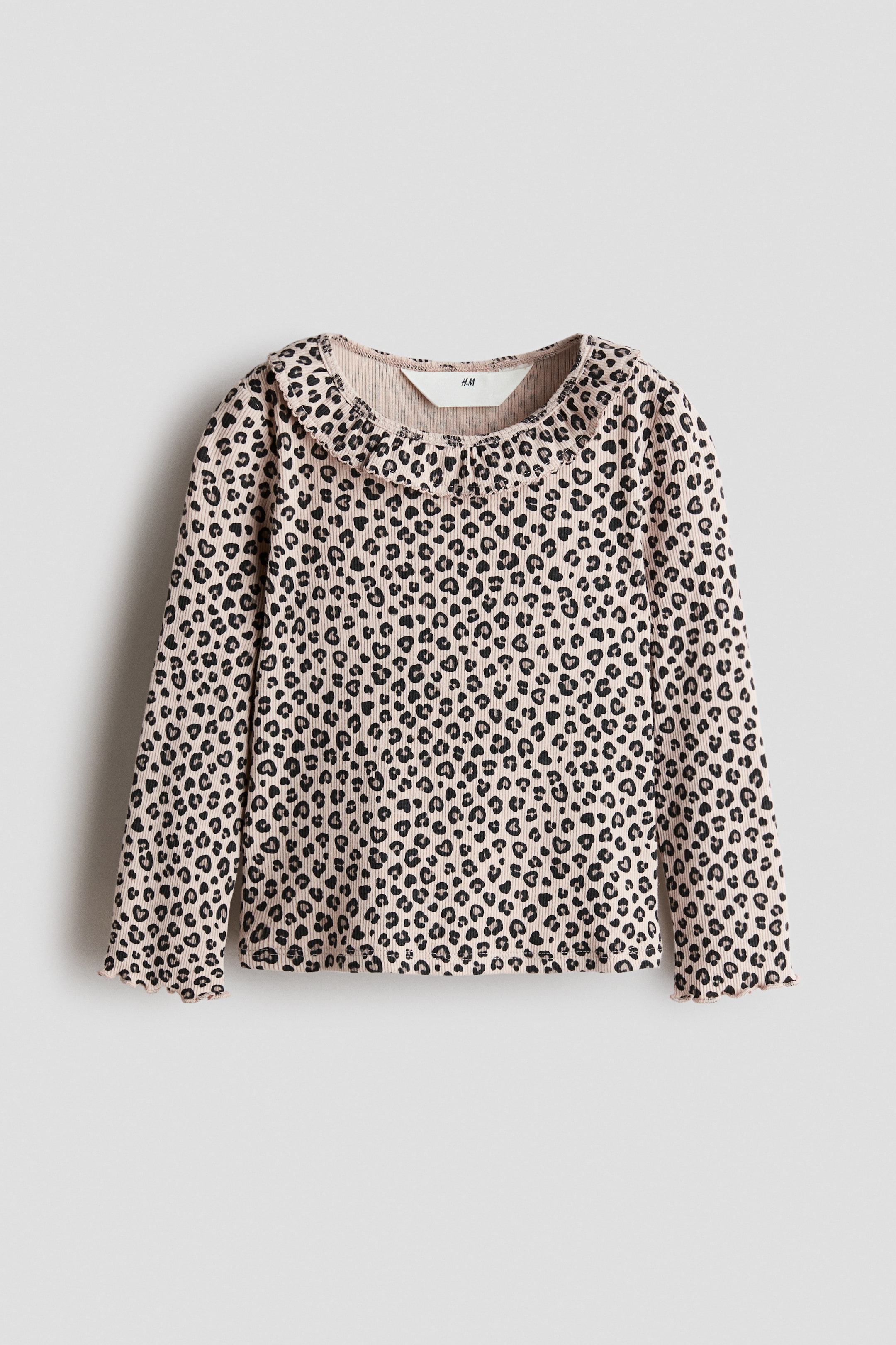 View larger image: A long-sleeved ribbed top is shown from the front, featuring an all-over black leopard-print pattern on a light pink fabric. The top has a ruffled collar and lettuce-edge hems at the cuffs.