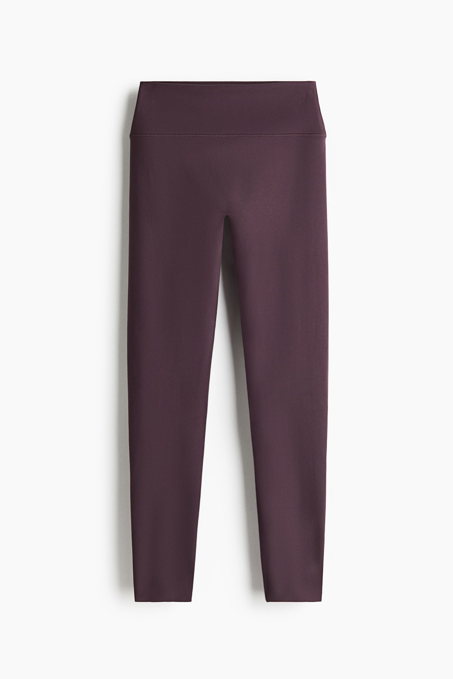 Se muestra un par de leggings de color morado oscuro desde un Ã¡ngulo frontal, con una cintura ancha de tiro alto y un diseÃ±o frontal liso y sin costuras. Las perneras ajustadas se estrechan hasta los tobillos, mostrando una estructura deportiva limpia y minimalista.