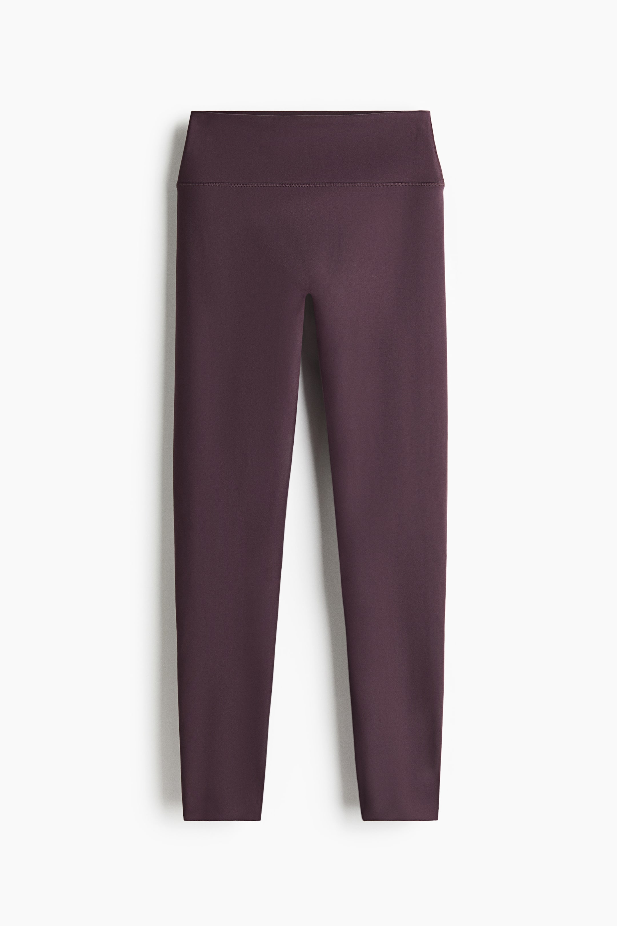 Agrandir l'image: Une paire de leggings violet foncé est présentée de face, avec une large taille haute et un devant lisse, sans coutures. Les jambes ajustées s’affinent jusqu’aux chevilles, mettant en valeur une structure sportive épurée et minimaliste.