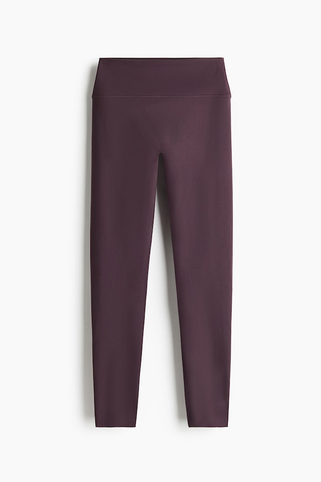 A pair of dark purple leggings is shown from a front-facing angle, featuring a wide, high-rise waistband and a smooth, seamless front design. The fitted legs taper down to the ankles, showcasing a clean, minimalist athletic structure. - 1