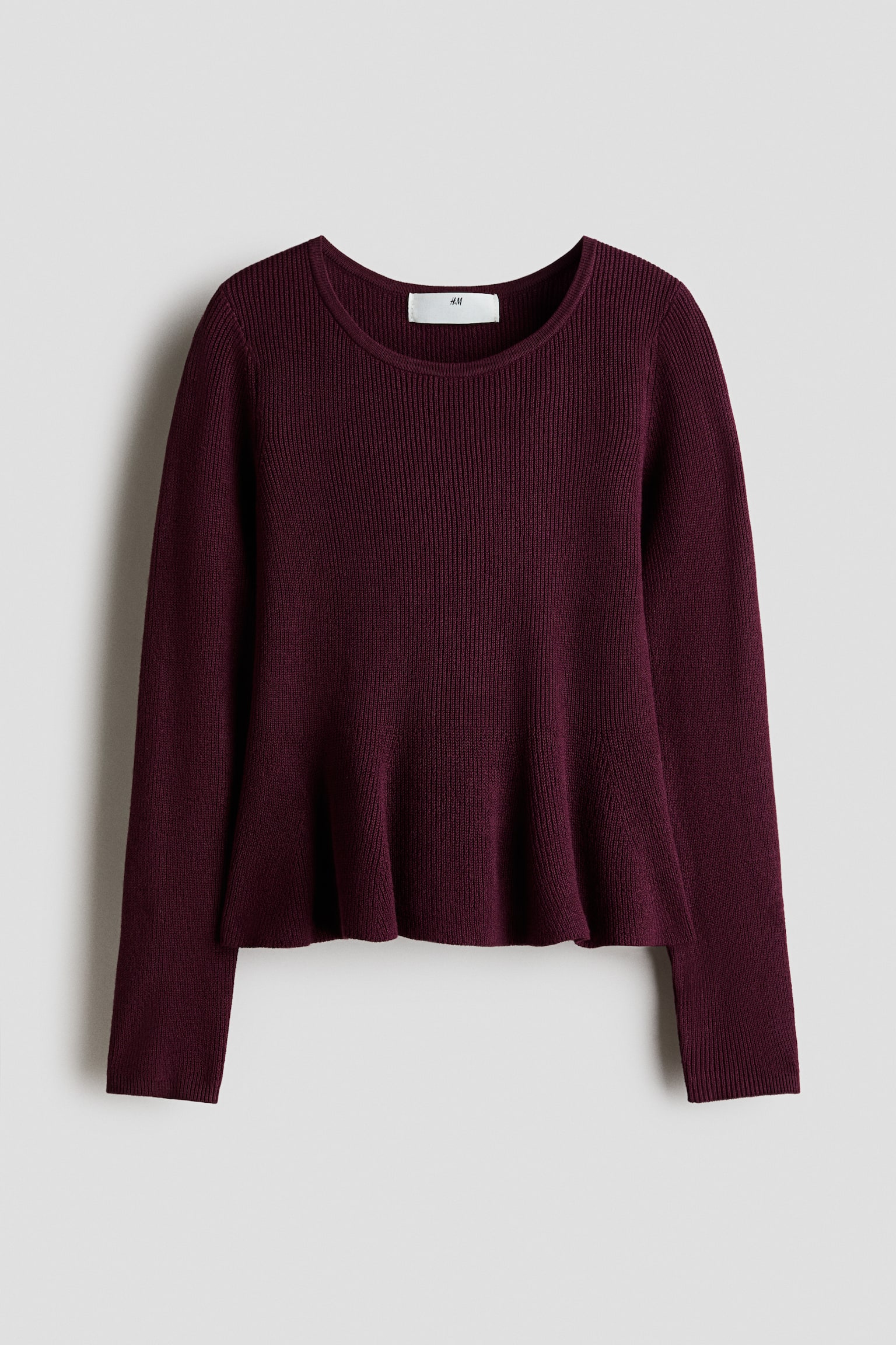 A burgundy ribbed-knit sweater is shown from the front, featuring a round neckline, long sleeves, and a flared peplum hem. The garment displays a fine vertical rib pattern throughout.