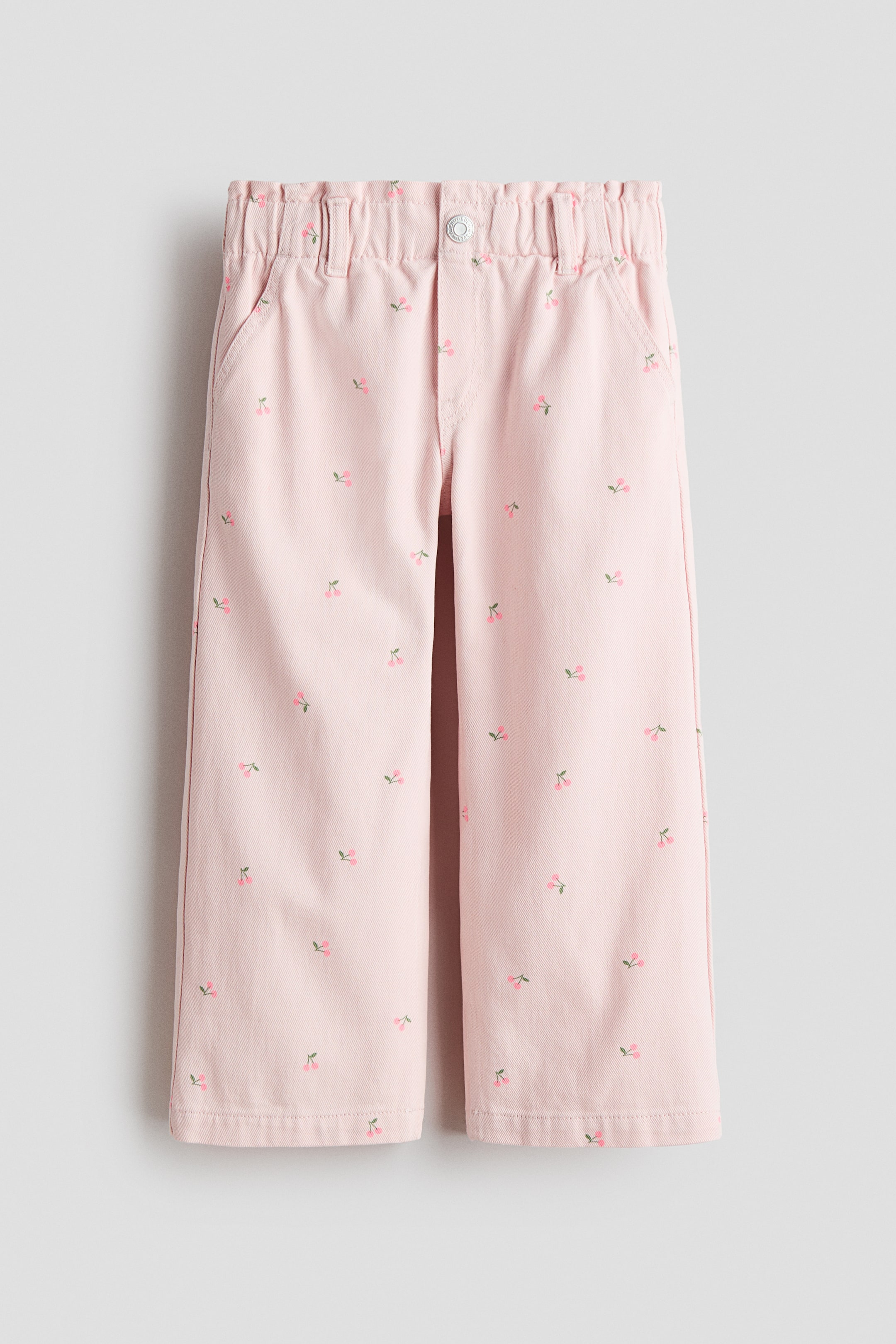 Büyük resmi görüntüle: Açık pembe pamuk denim kot pantolonlar FRONT görünümünde sunulur; geniş paçalı ve serpiştirilmiş kiraz motifine sahiptir. Lastikli paper bag bele, düğmeli sahte ön kapamaya ve çapraz yan ceplere sahip olacak şekilde tasarlanmıştır.