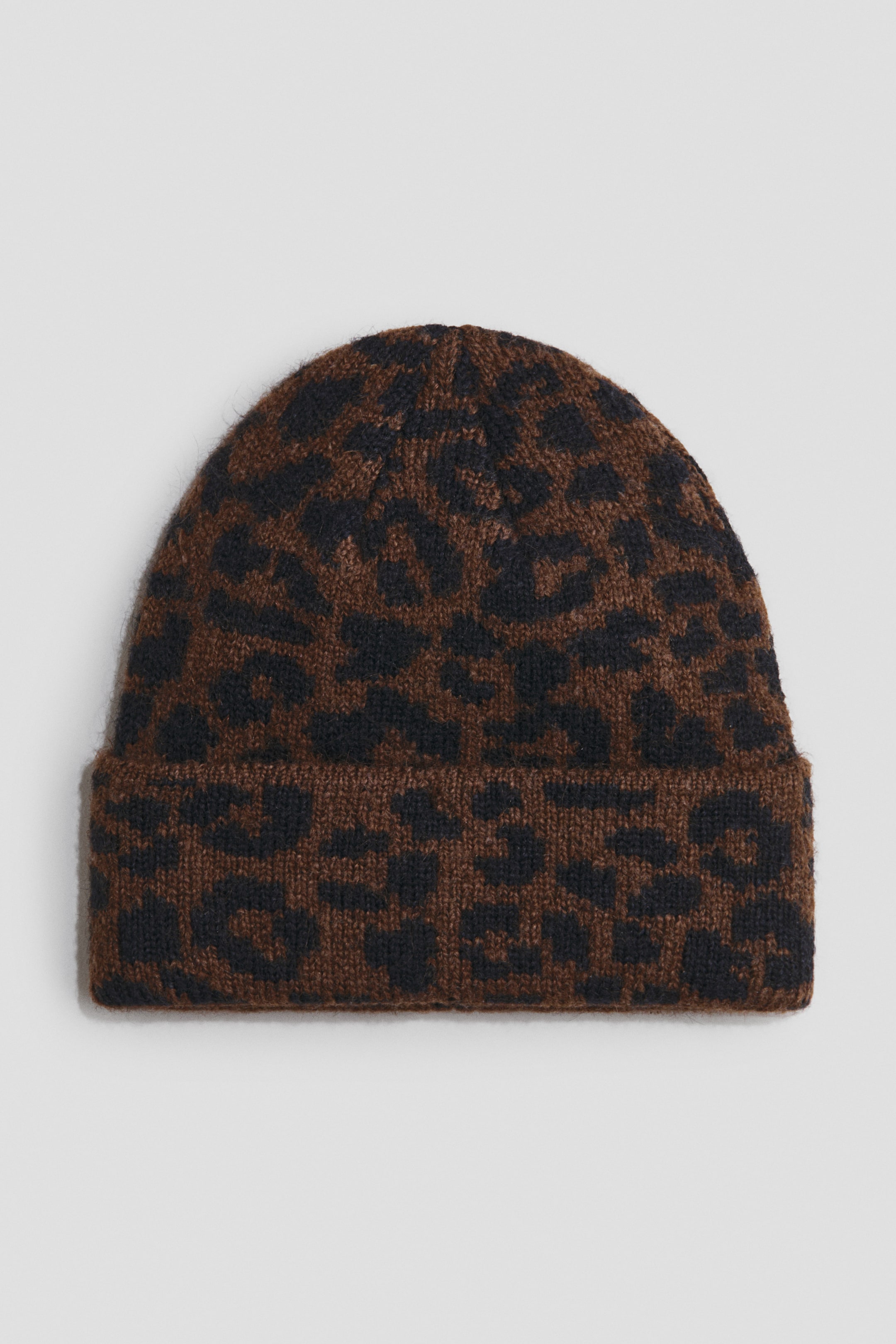 Voir une image plus grande: Un bonnet arbore un motif léopard brun et noir avec un rebord plié et une texture tricotée.