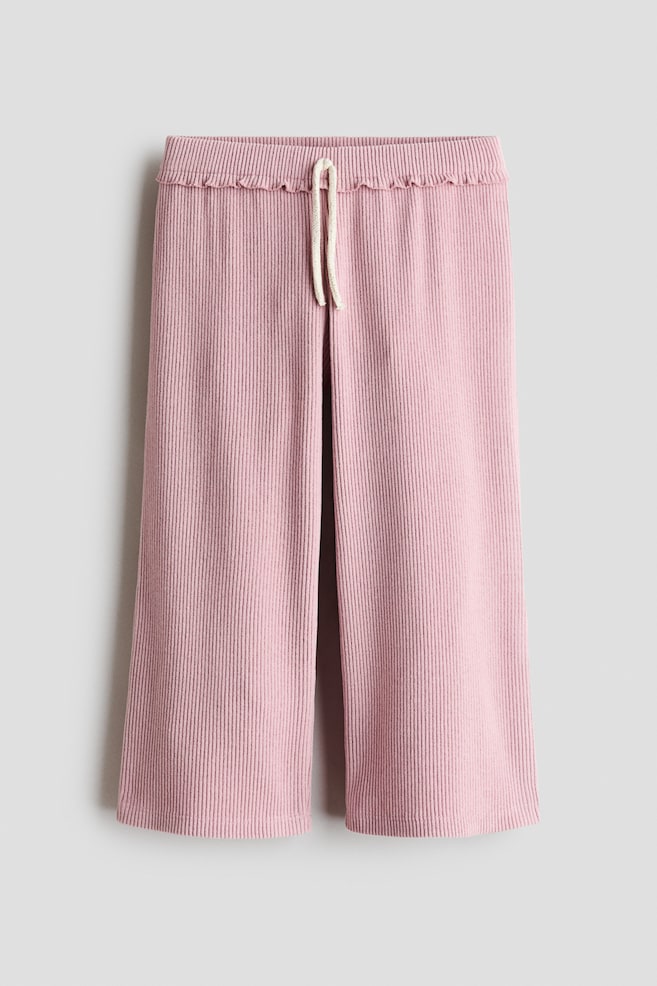 A pair of pink wide-leg trousers is hanging front-facing, showcasing a vertical ribbed texture throughout. The design features an elasticated waistband with a subtle ruffled trim and an off-white drawstring tied at the centre. - 1