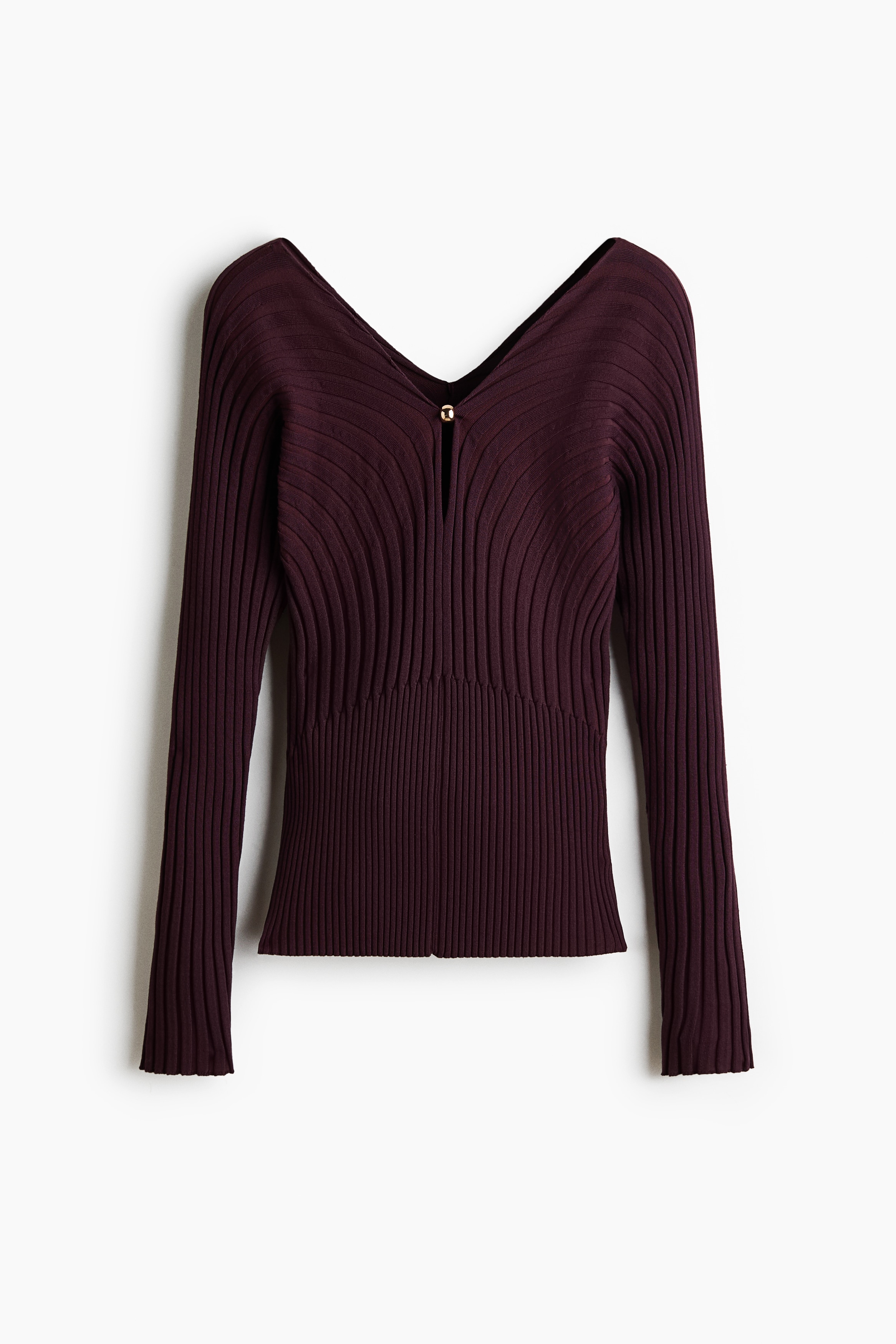 Un haut ajusté en maille côtelée, de couleur violet foncé et à manches longues, est porté par le mannequin, qui pose les bras croisés. Le haut présente un col en V avec une ouverture en goutte dâeau et un petit détail de perle métallique de couleur dorée sur le devant.