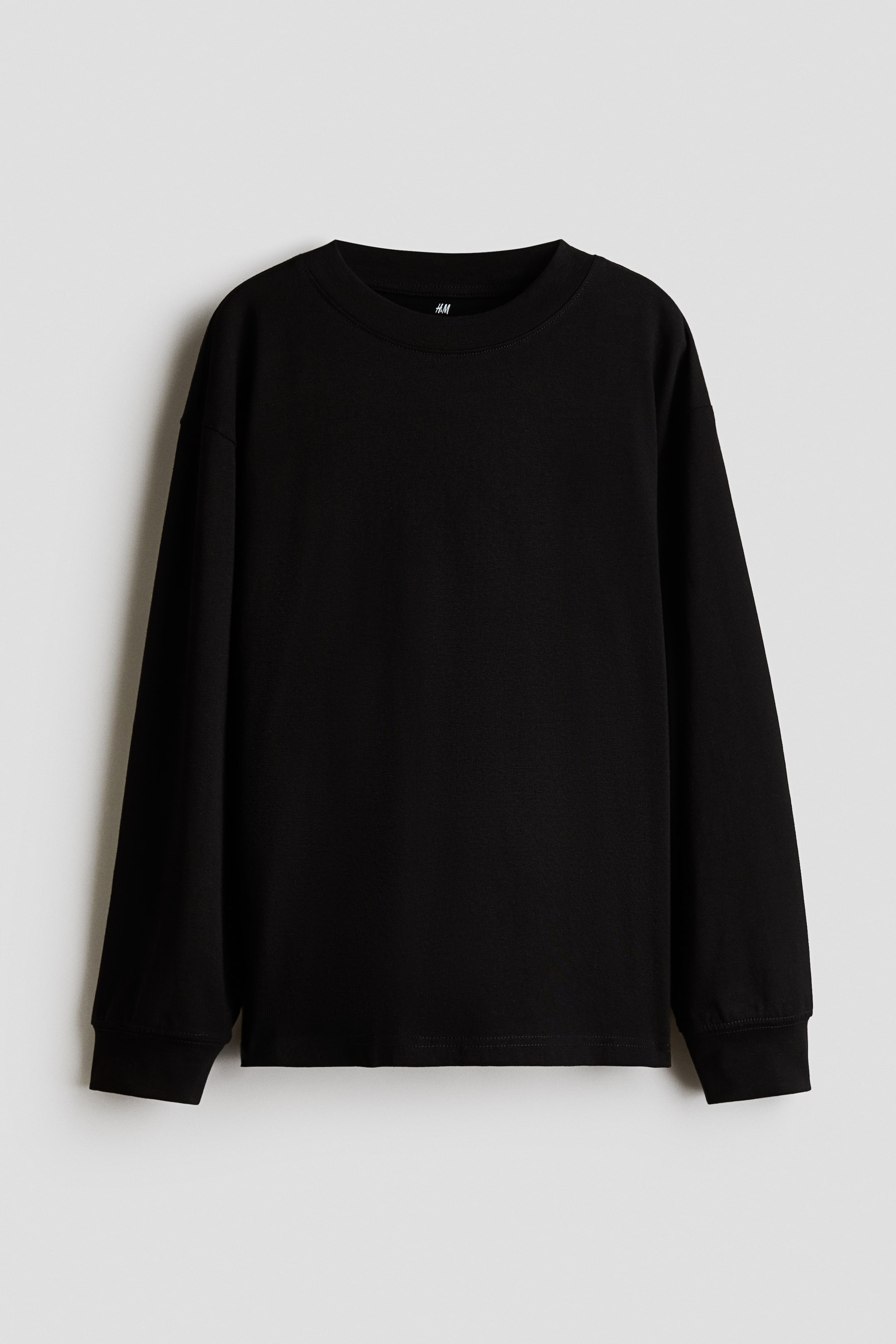 View larger image: A black, loose-fit long-sleeve tee is shown from the front, featuring a round, rib-trimmed neckline, dropped shoulders, ribbed cuffs, and a straight-cut hem.