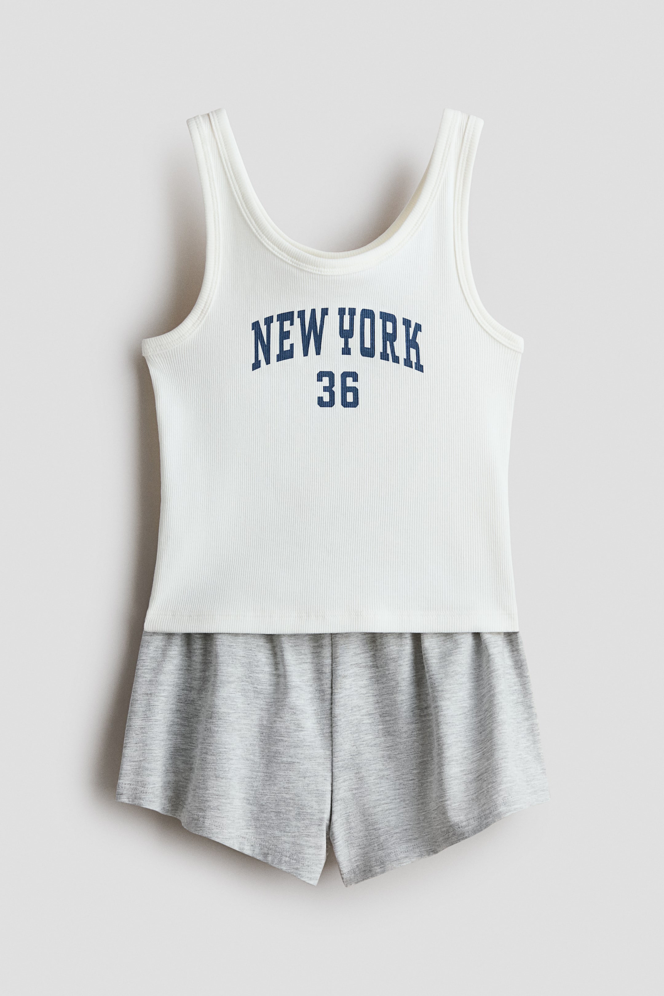 View larger image: Pyjamas featuring a white ribbed vest top, displaying 'NEW YORK 36' printed in dark blue on its front, and finished with binding around the neckline and armholes. It is paired with grey jersey shorts, which feature an elasticated waist, all presented from the front.
