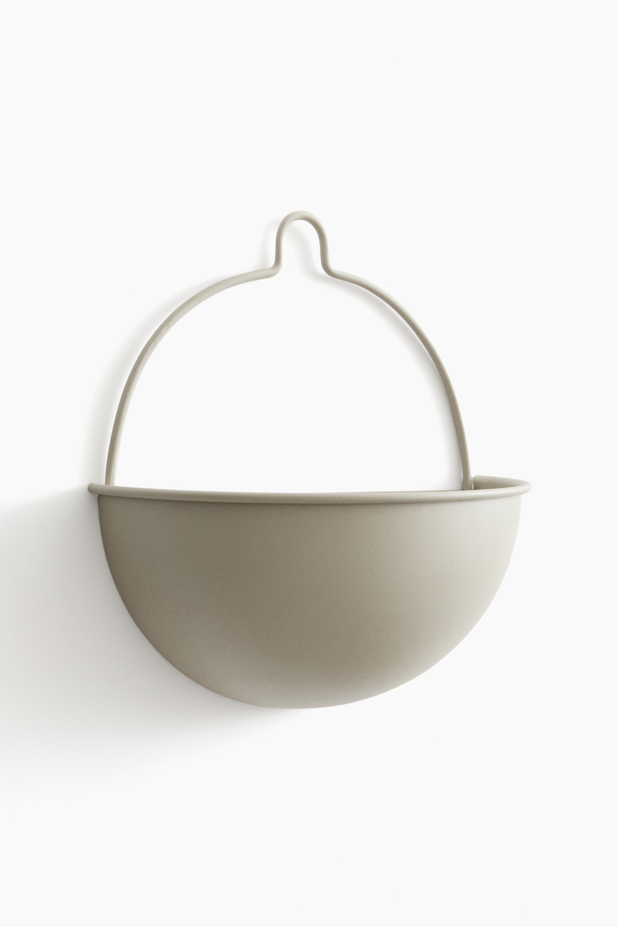 View larger image: "This wall-mounted plant pot is showcased from the front, boasting a half-moon shape crafted from painted metal, finished in a matte, light gray-beige hue, and equipped with a semi-circular hanging handle."