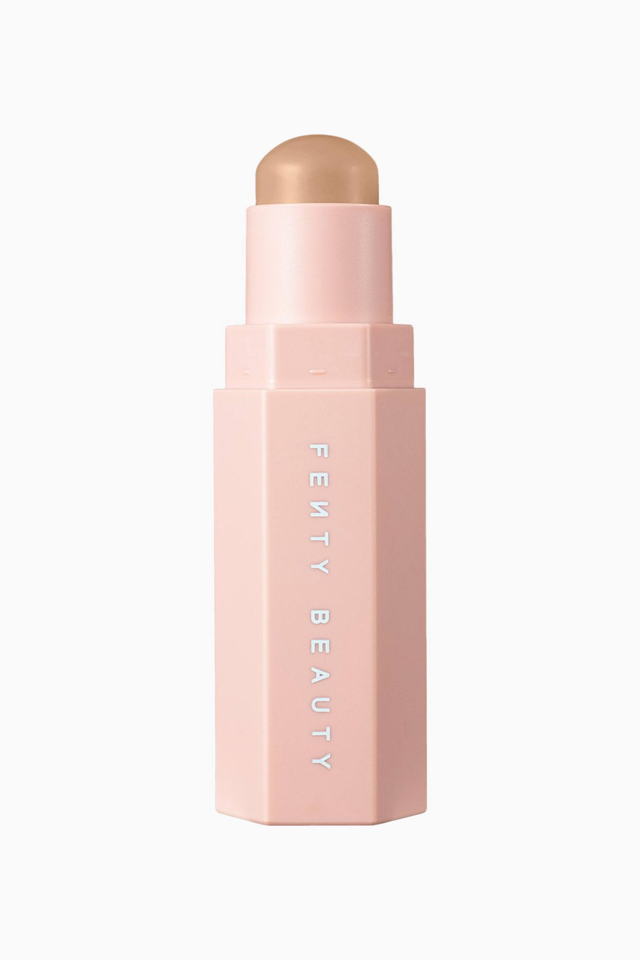 Visa större bild: En Fenty Beauty-contourstick står upprätt och visar ett sexkantigt, ljusrosa hölje med varumärkesnamnet tryckt vertikalt i vitt. En kupolformad, ljusbeige krämig makeupstick sticker upp från toppen av tuben.