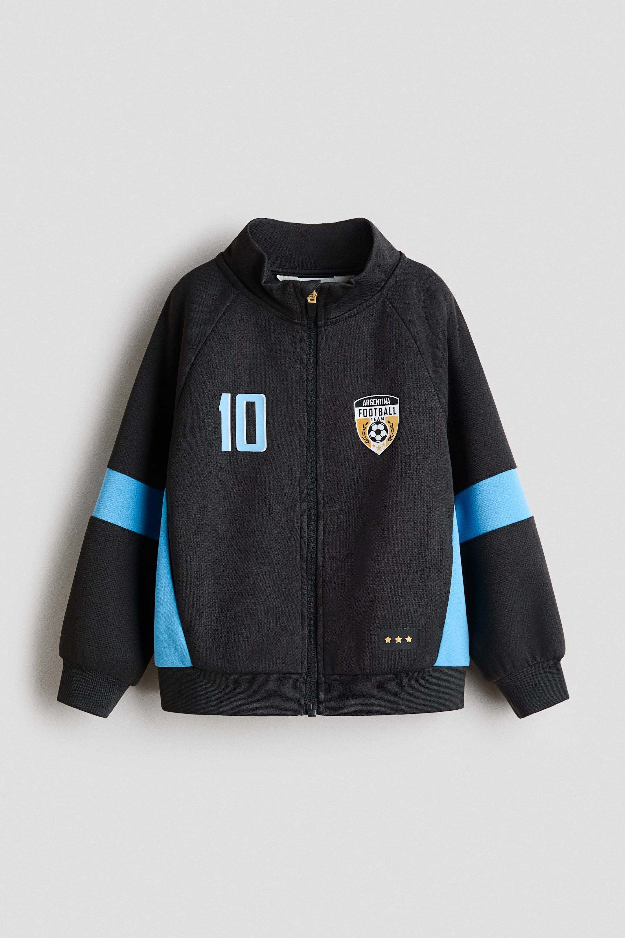 View larger image: The black track jacket, seen from the front, features a slight sheen, a stand-up collar and a full-zip closure. It displays light-blue panels along the raglan sleeves and sides, ribbed cuffs and hem, a light-blue number '10' on the left chest, an 'Argentina Football Team' crest on the right, and three gold stars near the hem.