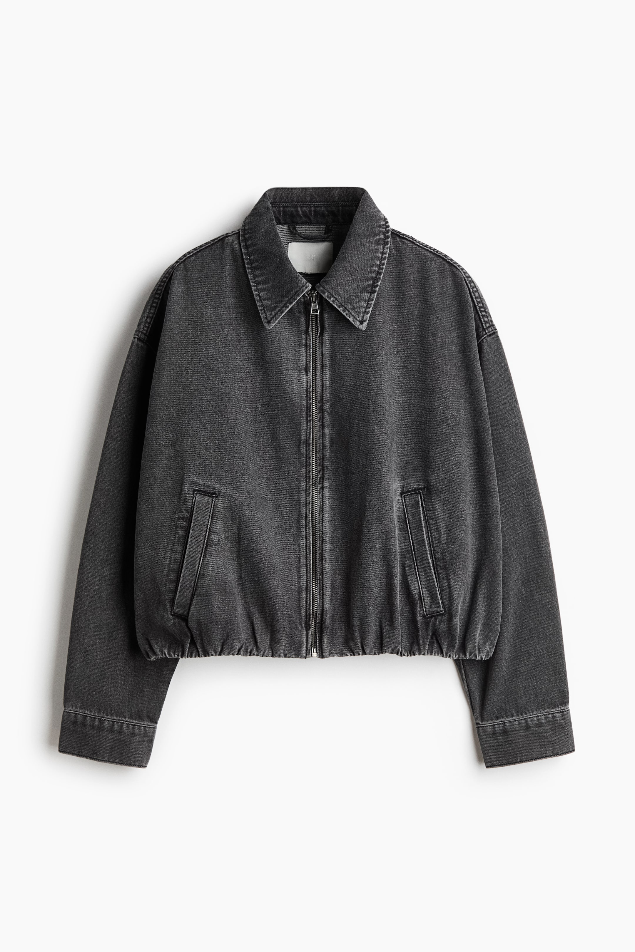 הצגת תמונה גדולה יותר: ז'קט ג'ינס קצר ואוברסייז בצבע אפור כהה מציג את חלקו הקדמי, הכולל צווארון, סגירת רוכסן לאורך החזית וכתפיים שמוטות. הוא מציג שרוולים ארוכים עם חפתים מכופתרים, כיסי צד קדמיים ותחתית מכווצת וגמישה היוצרת צללית מרובעת.