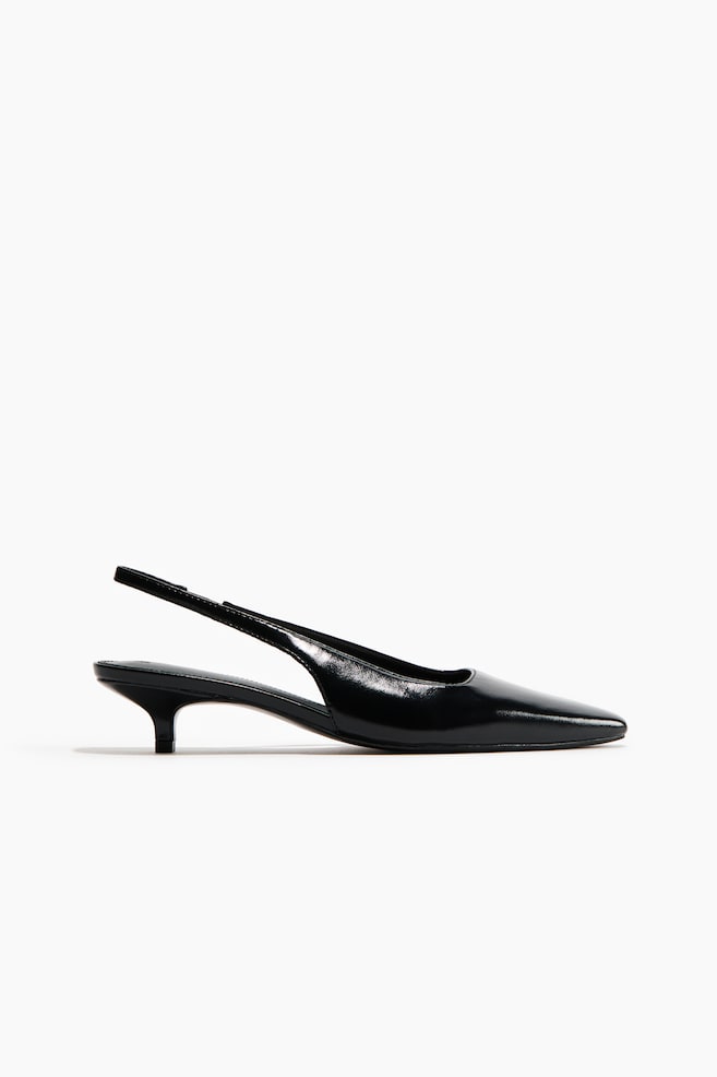 A black slingback shoe features a pointed toe, a thin slingback strap and a kitten heel. The material has a glossy finish. - 1