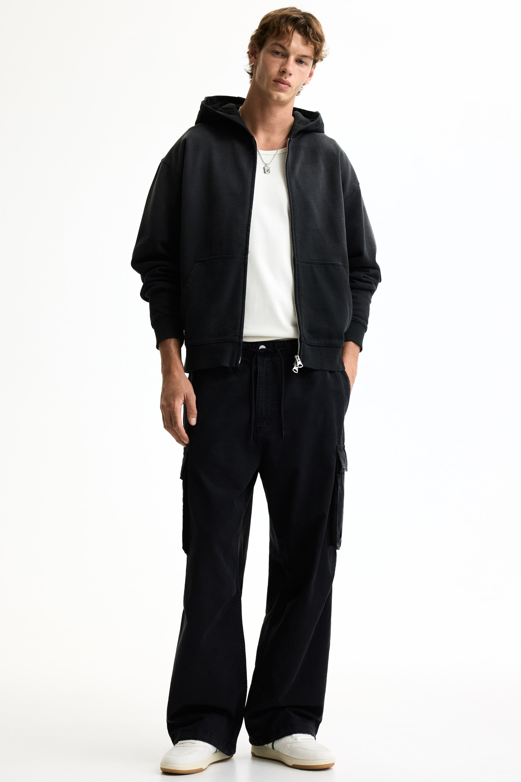 View larger image: A black zip-up hoodie is showcased from the front, highlighting an oversized fit, a hood, and ribbed cuffs and hem. The full-length zipper is open, revealing a white ribbed top underneath, and it features front patch pockets.
