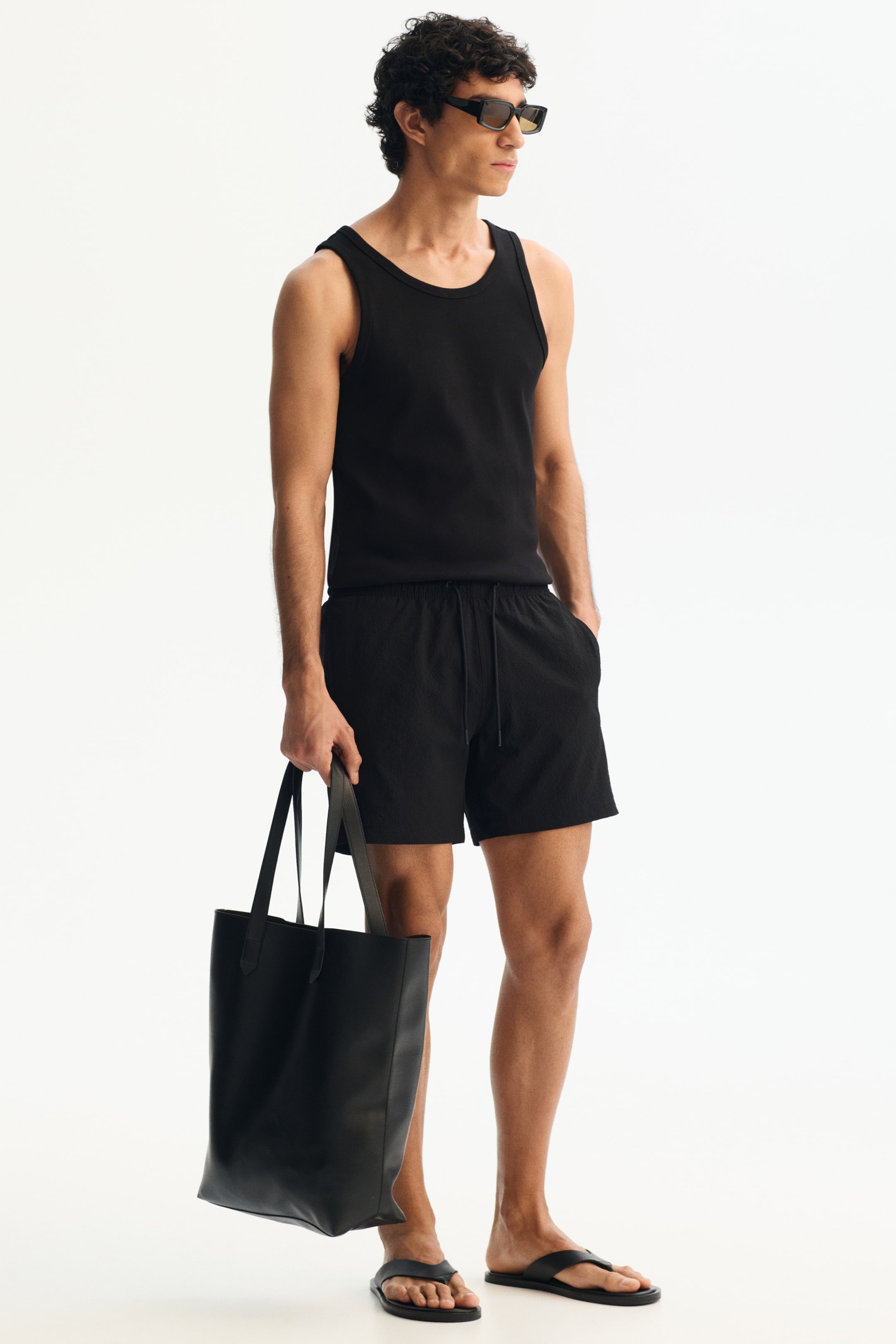 View larger image: The model is wearing mid-length swim shorts crafted from a textured weave. These shorts come with a drawstring waist and subtle side pockets, one of which holds the model's hand.