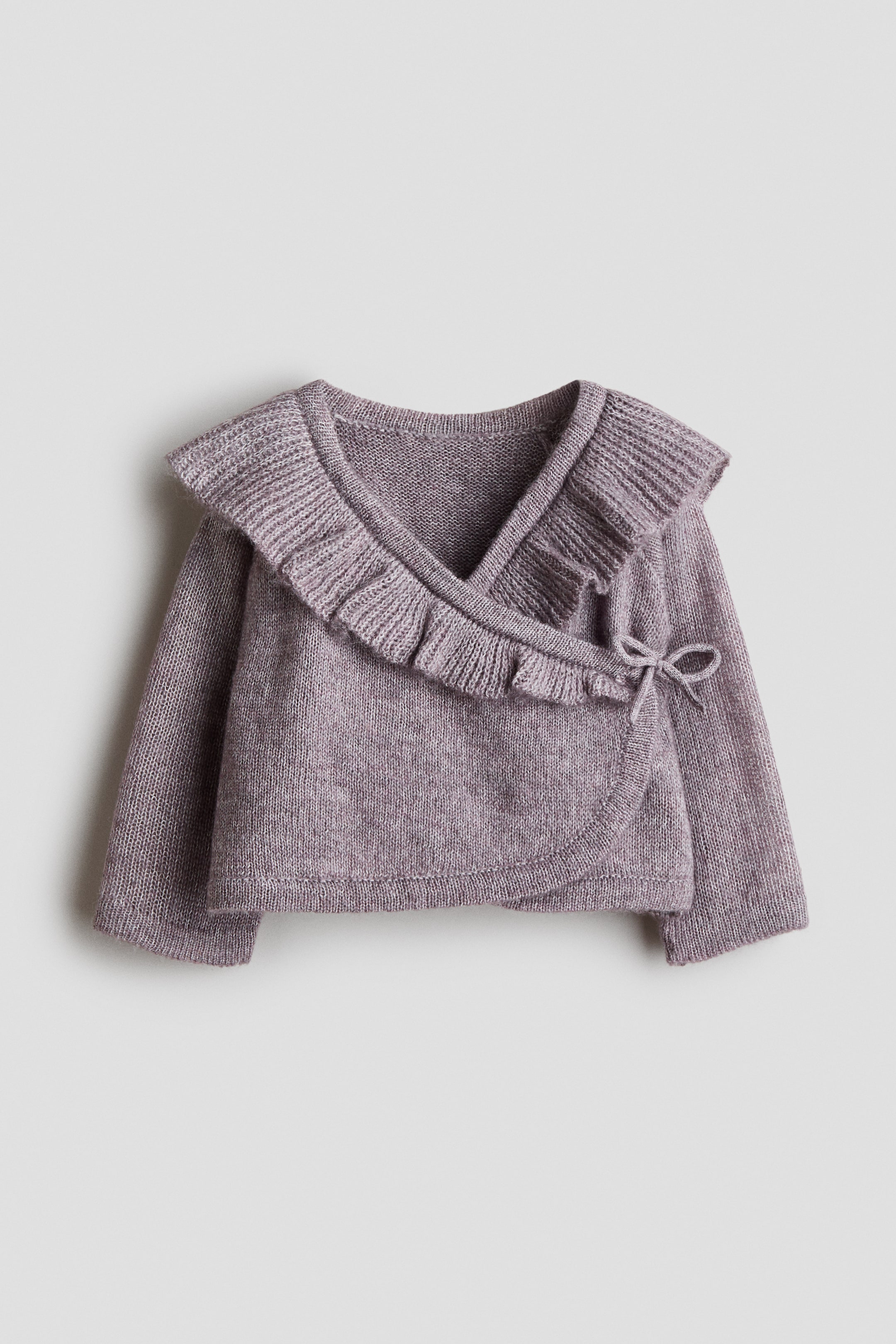 View larger image: A light purple cardigan is shown from the front, made from a soft, fine knit. It features a wrapover front with a decorative tie detail and concealed press studs at the sides, and is designed with a V-shaped neckline with a ribbed frill trim and long sleeves.