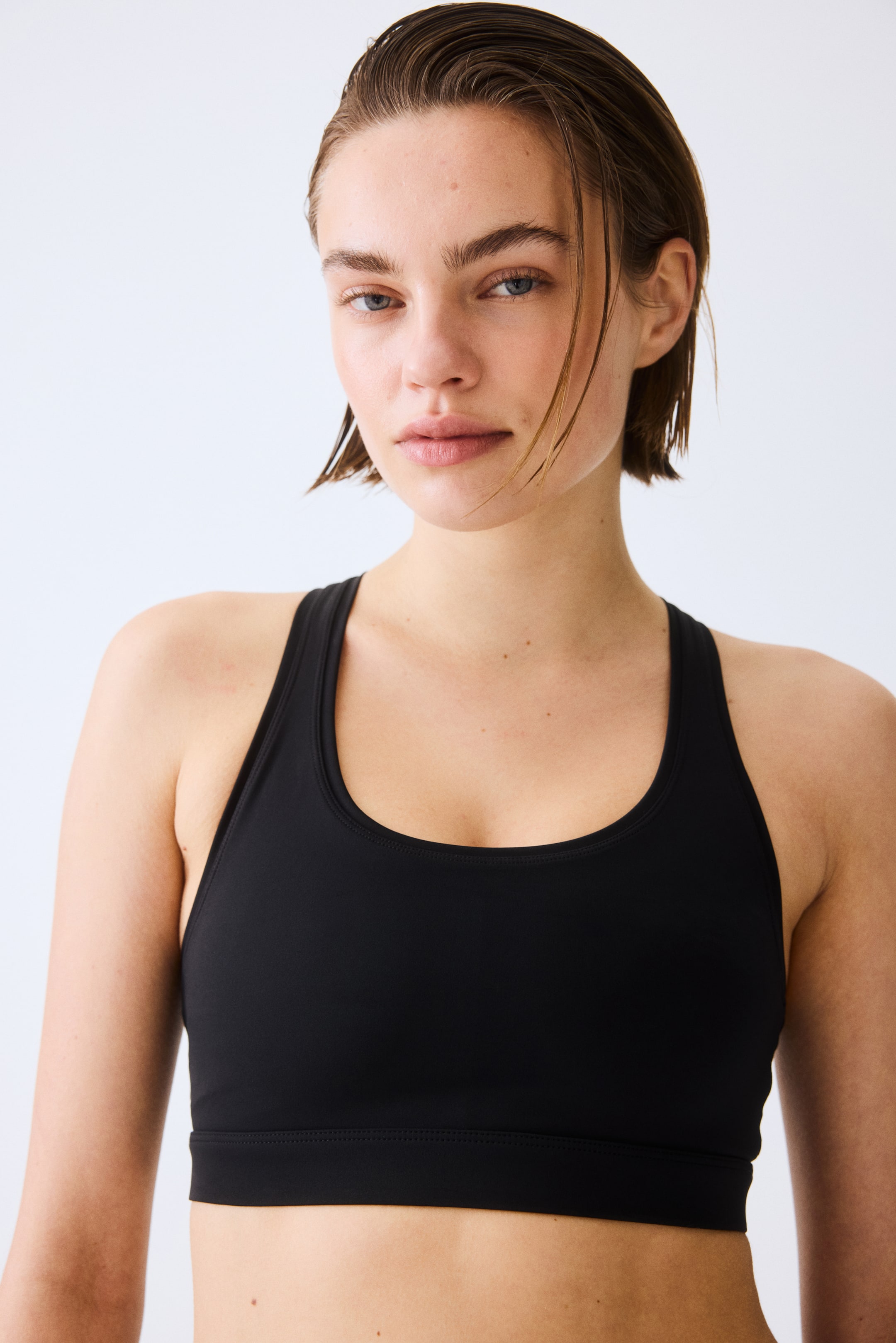 View larger image: A black sports bra is facing forward, featuring a scoop neck, racerback straps, and a wide elasticated band under the bust.