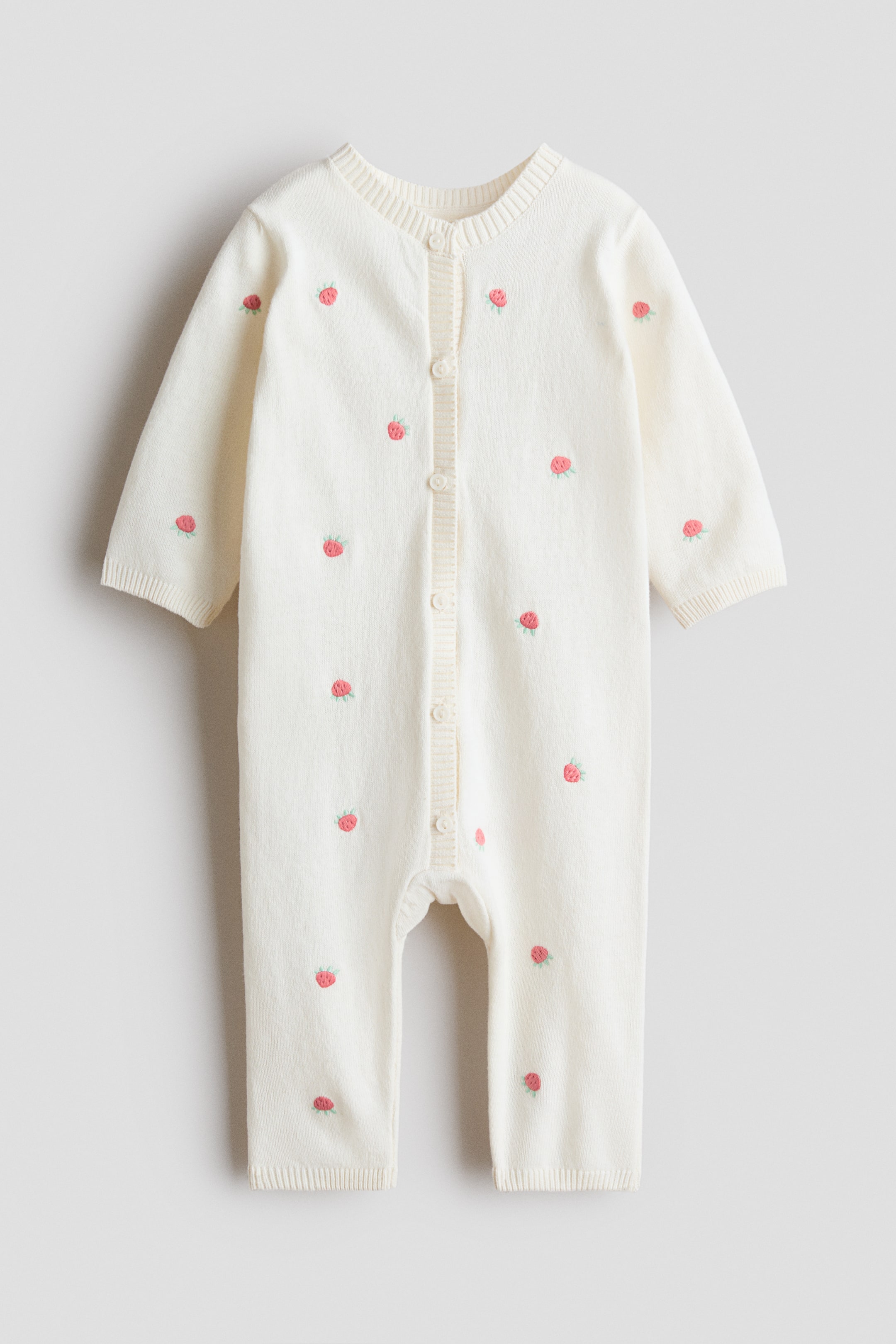 View larger image: "A romper suit in a soft cotton knit is facing front, featuring a round ribbed neckline and buttons extending down the front. This cream-coloured suit is adorned with embroidered strawberry motifs throughout, and its long sleeves and full-length legs are ending in ribbed cuffs."