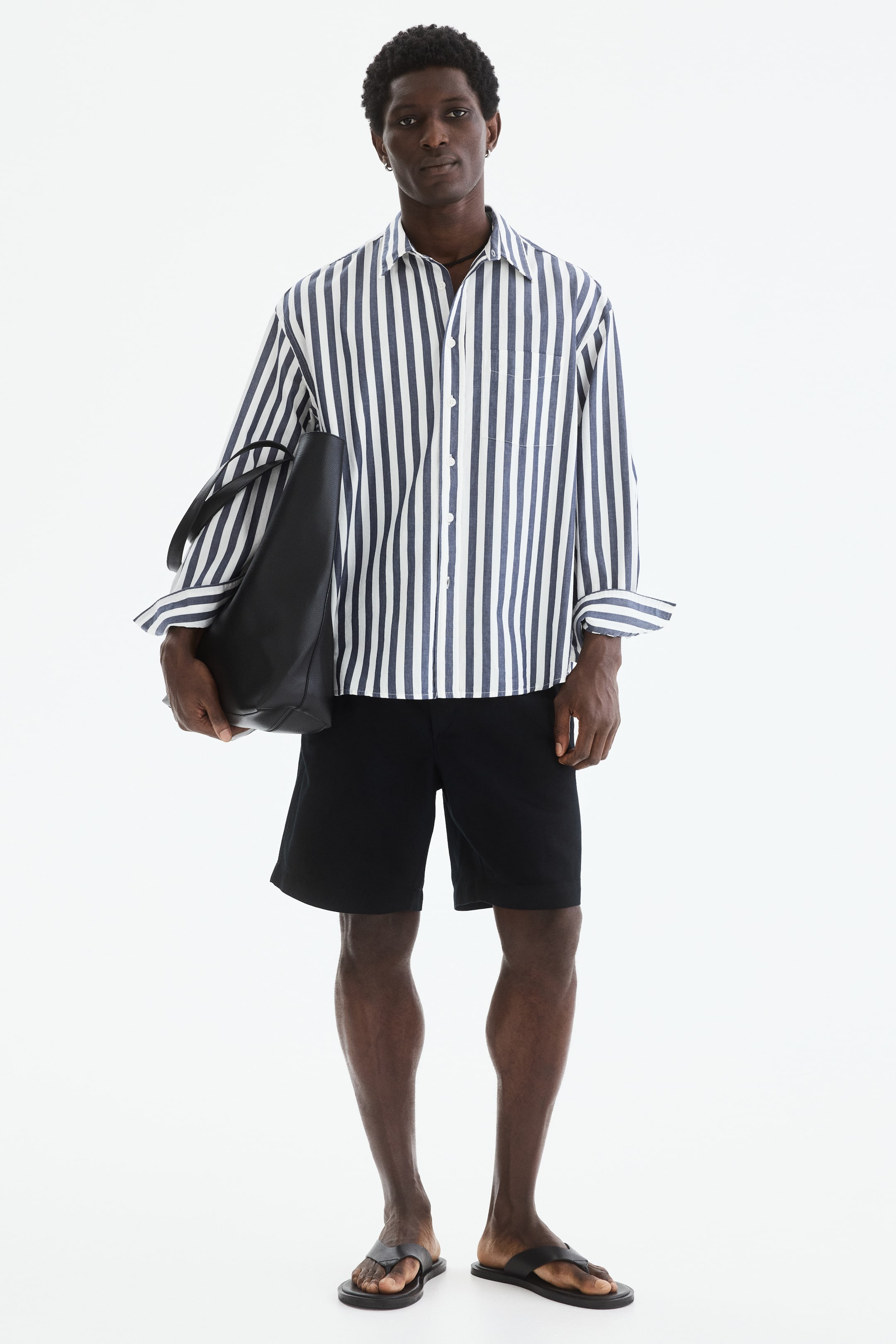 View larger image: The model is wearing black shorts with a relaxed fit. These shorts sit above the knee, and the model is carrying a black tote bag.