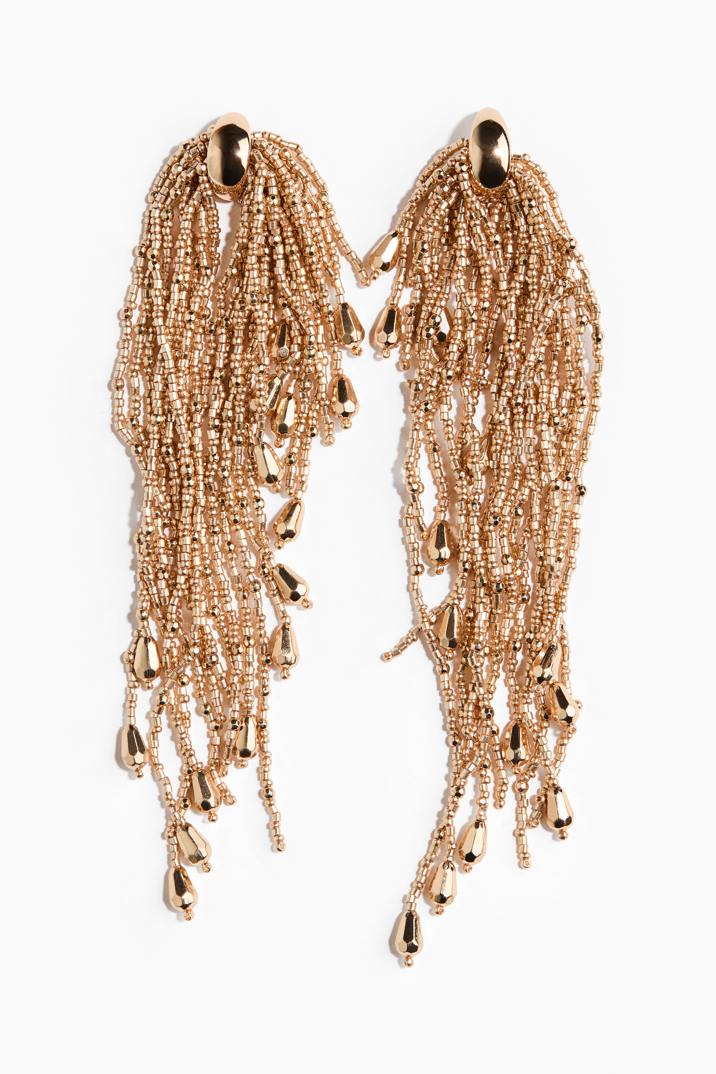 Gold-toned dangling earrings with a small metal hoop top and long, cascading strands of tiny beads are being worn by the model. The shoulder-length strands, ending in small teardrop-shaped beads, drape towards the collarbone against a white off-the-shoulder top.
