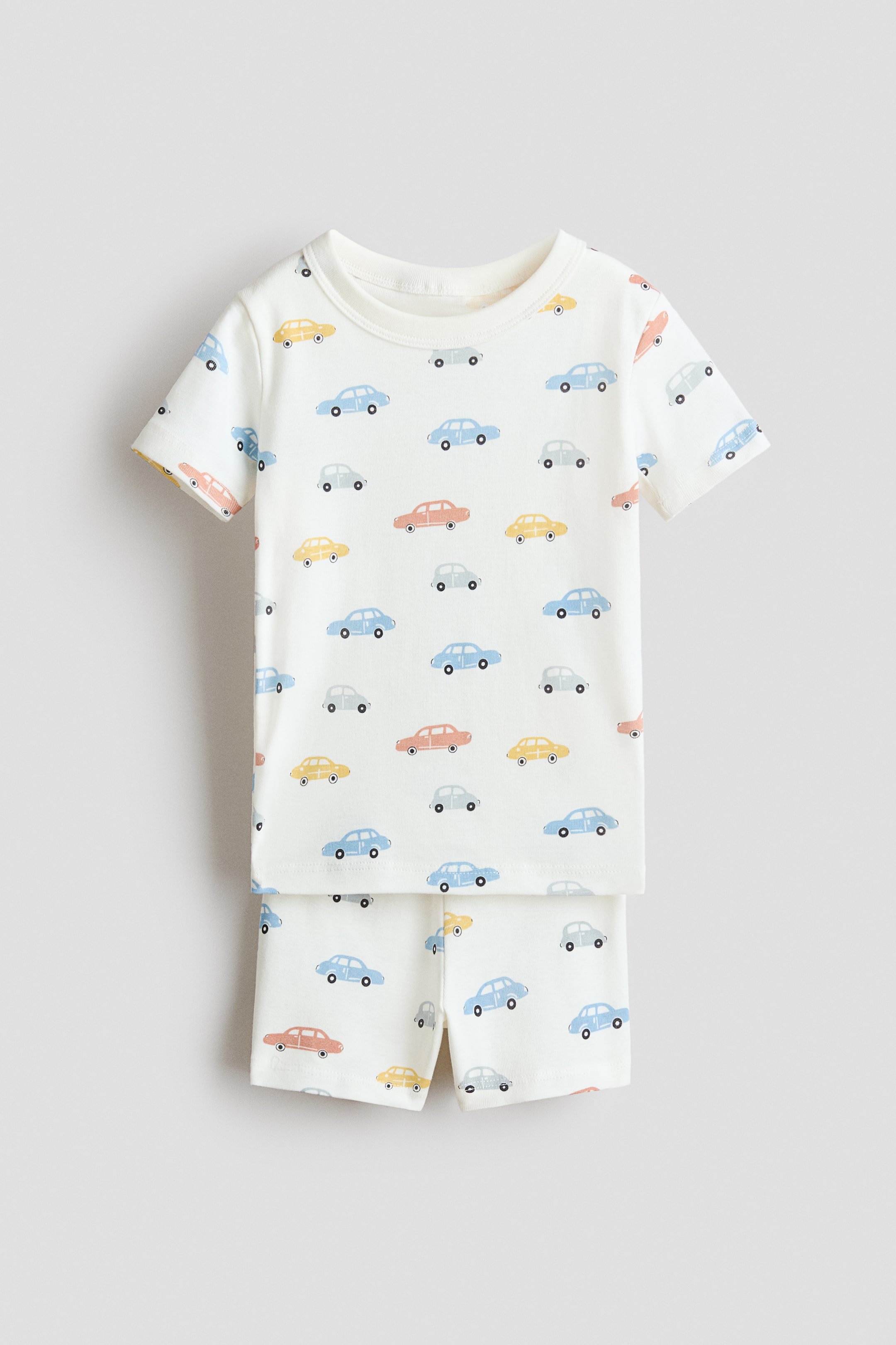 View larger image: A pajama T-shirt and shorts set is shown in a front view, featuring a cream base with an all-over print of small cars in light blue, yellow, orange, and gray. The short-sleeve T-shirt features a rib-trimmed neckline, and the matching shorts have an elastic waistband.