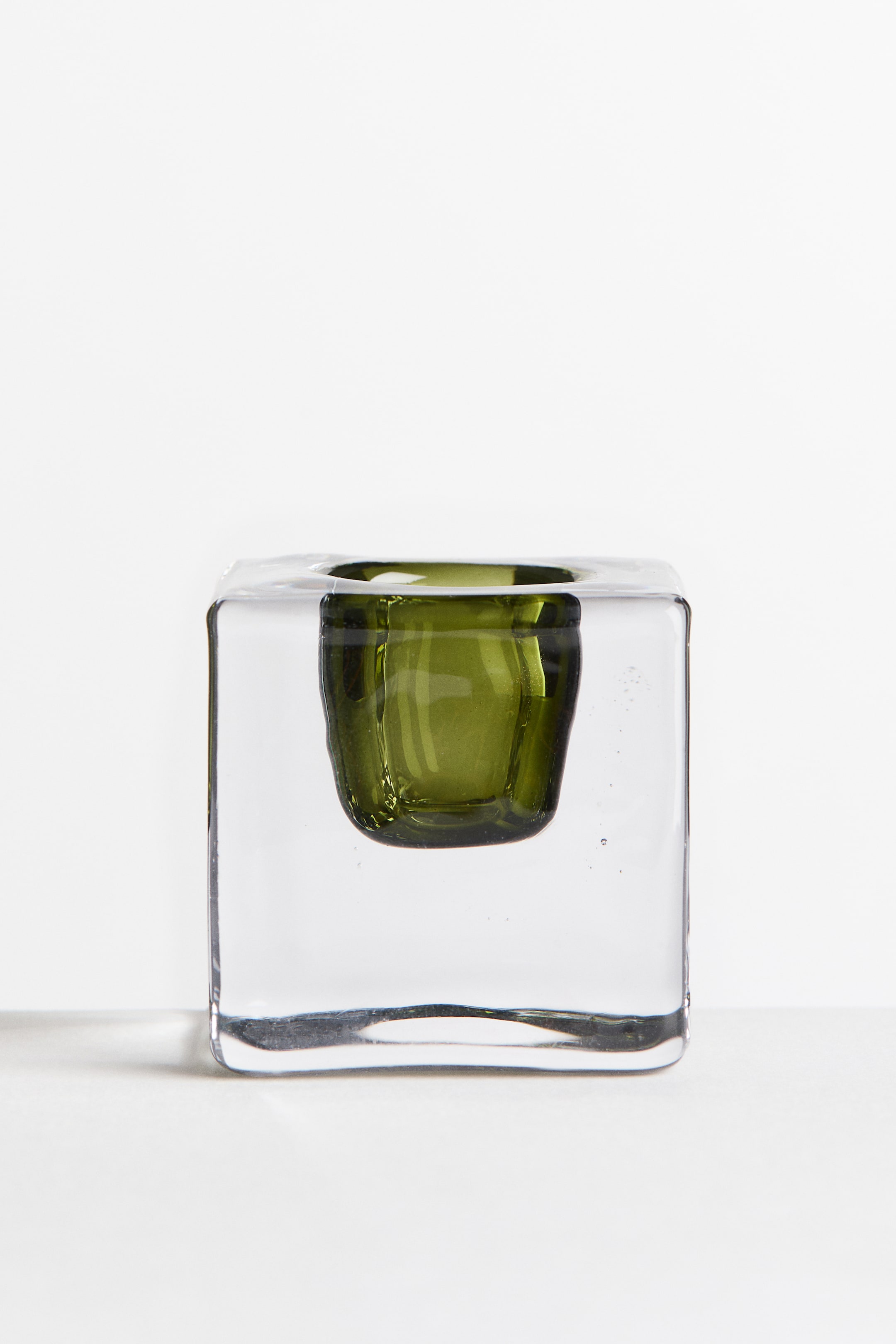 View larger image: A small candlestick features a thick, clear glass cube body with an embedded olive-green glass socket.