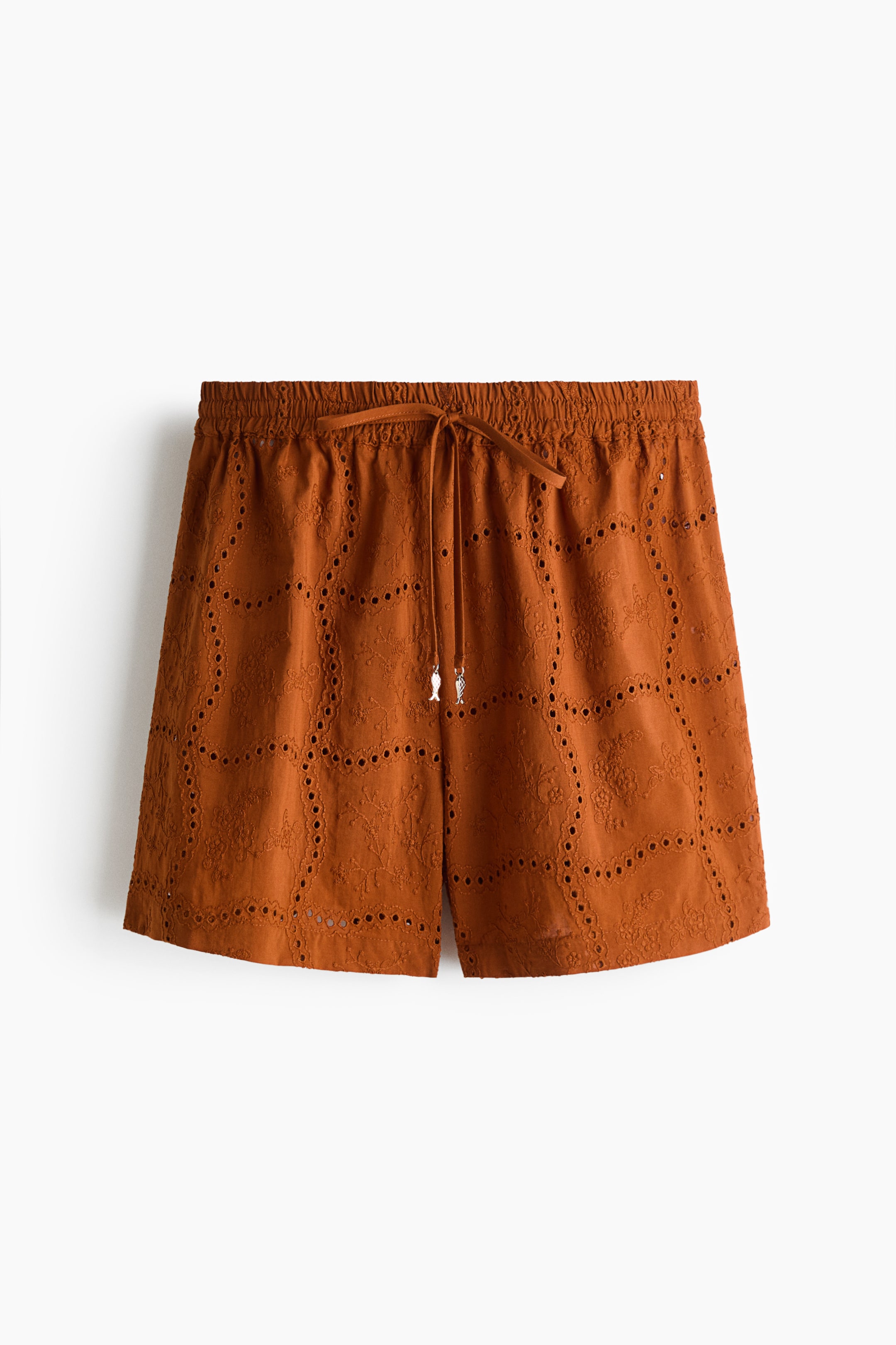 View larger image: Brownish-orange shorts, shown from the front, feature an elasticated waistband with a drawstring ending in two silver-toned charms, and display intricate eyelet embroidery in repeating floral and geometric patterns across the fabric.