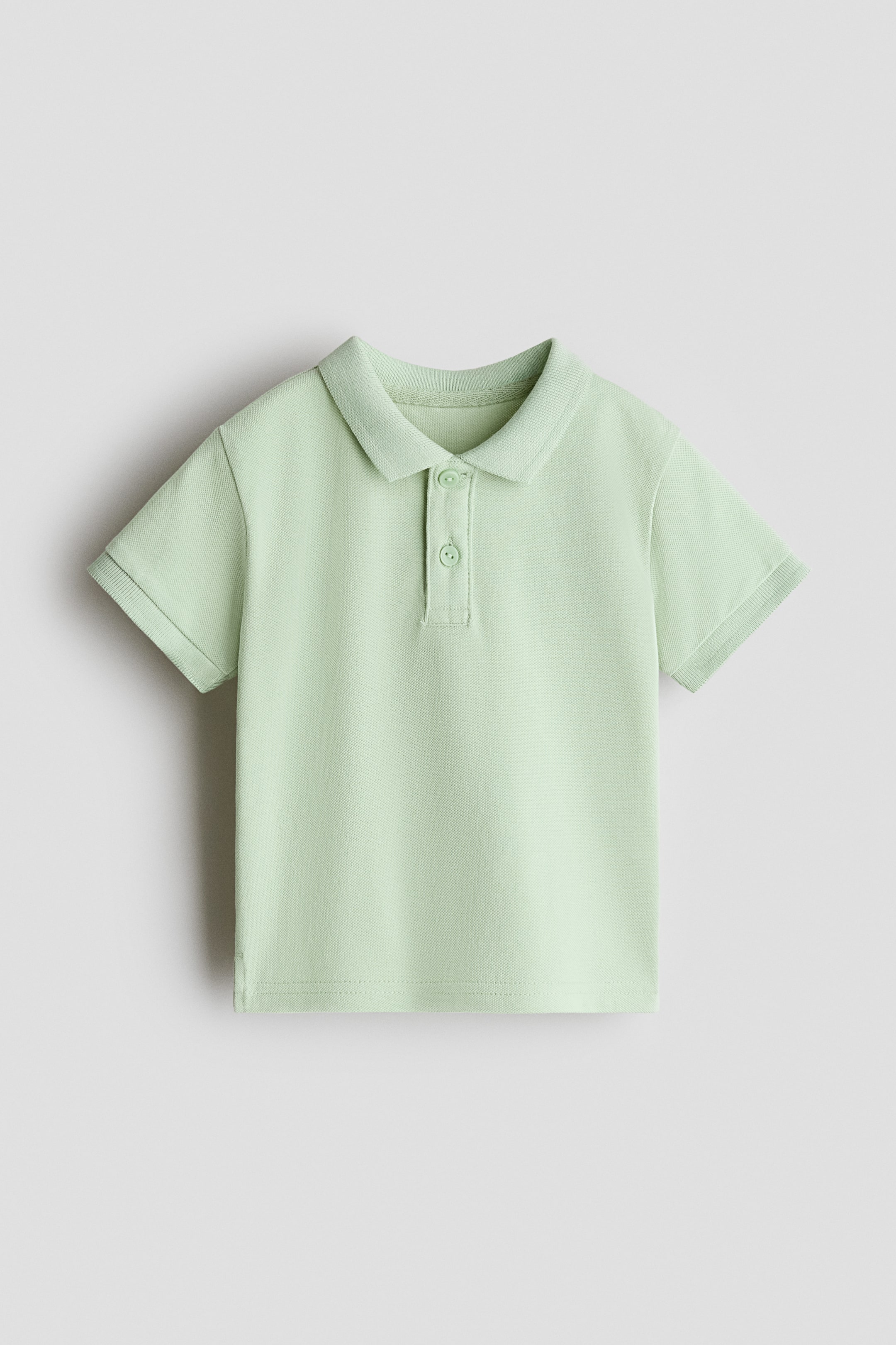 View larger image: A light green pique knit polo shirt features a classic collar, a two-button placket, and ribbed short sleeves.