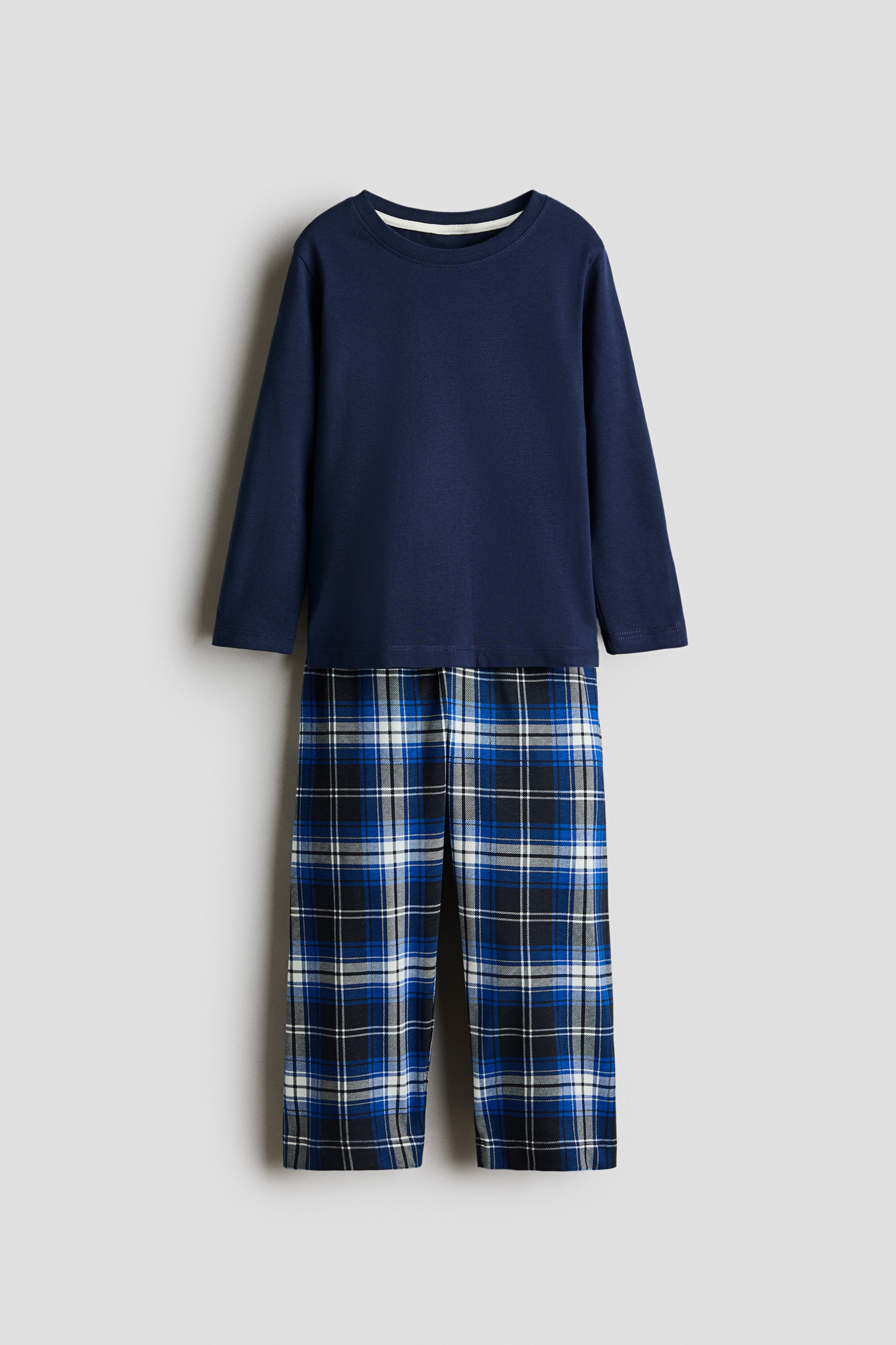 View larger image: A two-piece pajama set featuring a navy blue long-sleeved top with a round neckline and matching blue, black, and white plaid pants.