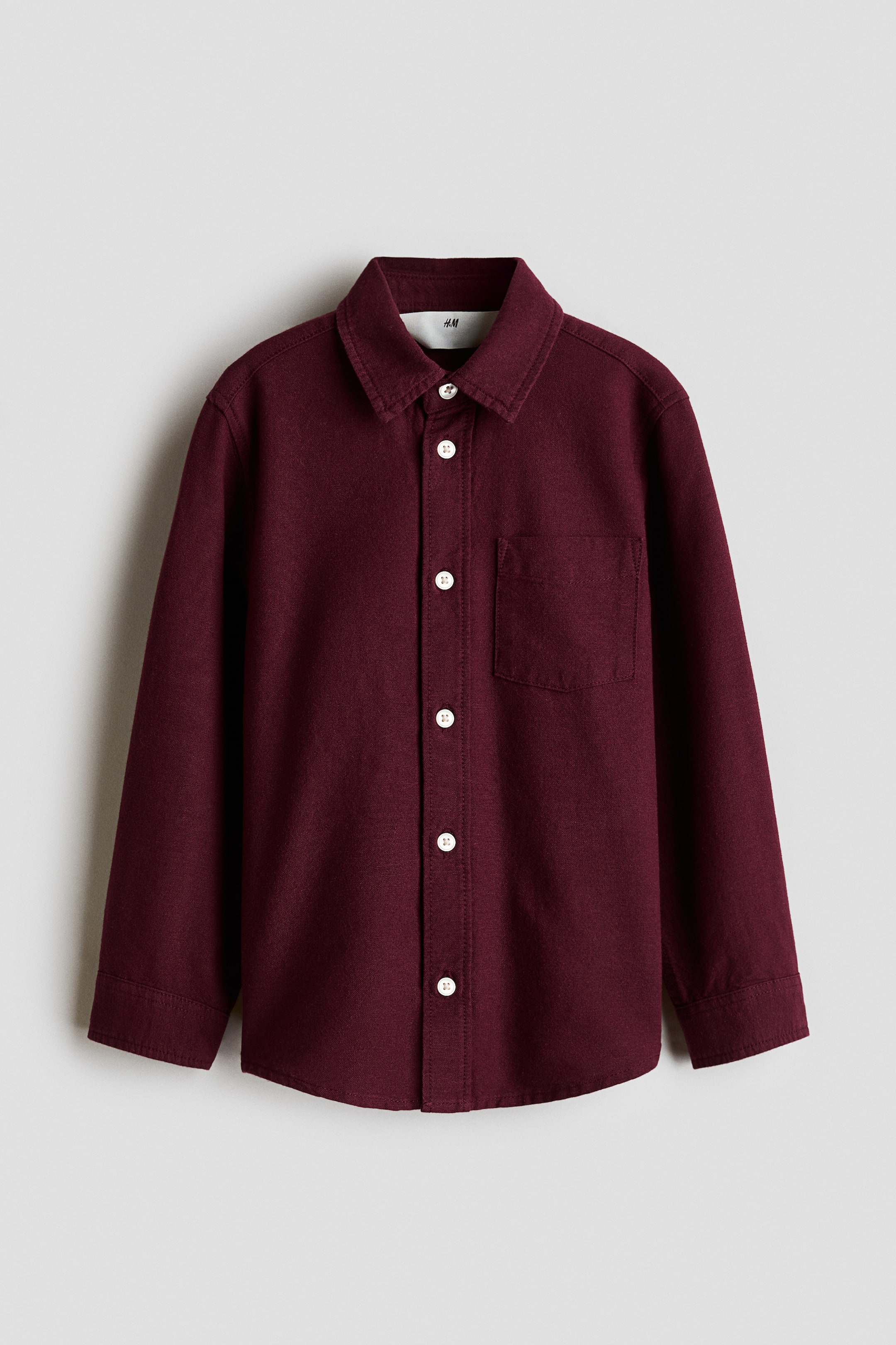 View larger image: A maroon Oxford cotton shirt is shown facing front, featuring a turn-down collar and a full button-down front with white buttons. It has long sleeves with sleeve plackets and buttoned cuffs, a patch chest pocket on the left side, and a rounded hem.