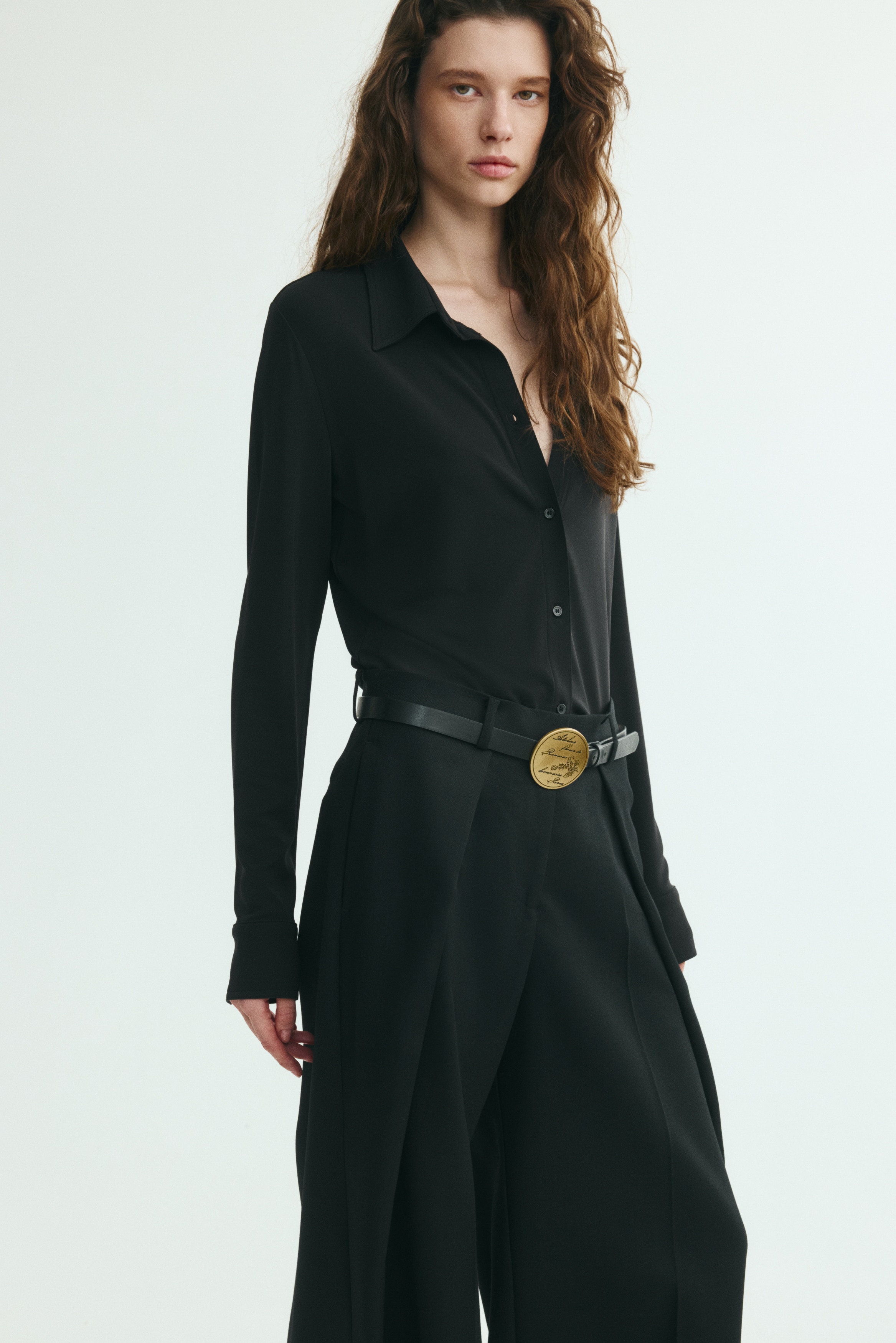 A black fitted shirt is hanging front-facing, showcasing a pointed collar, a central button fastening, and long sleeves with wide cuffs.