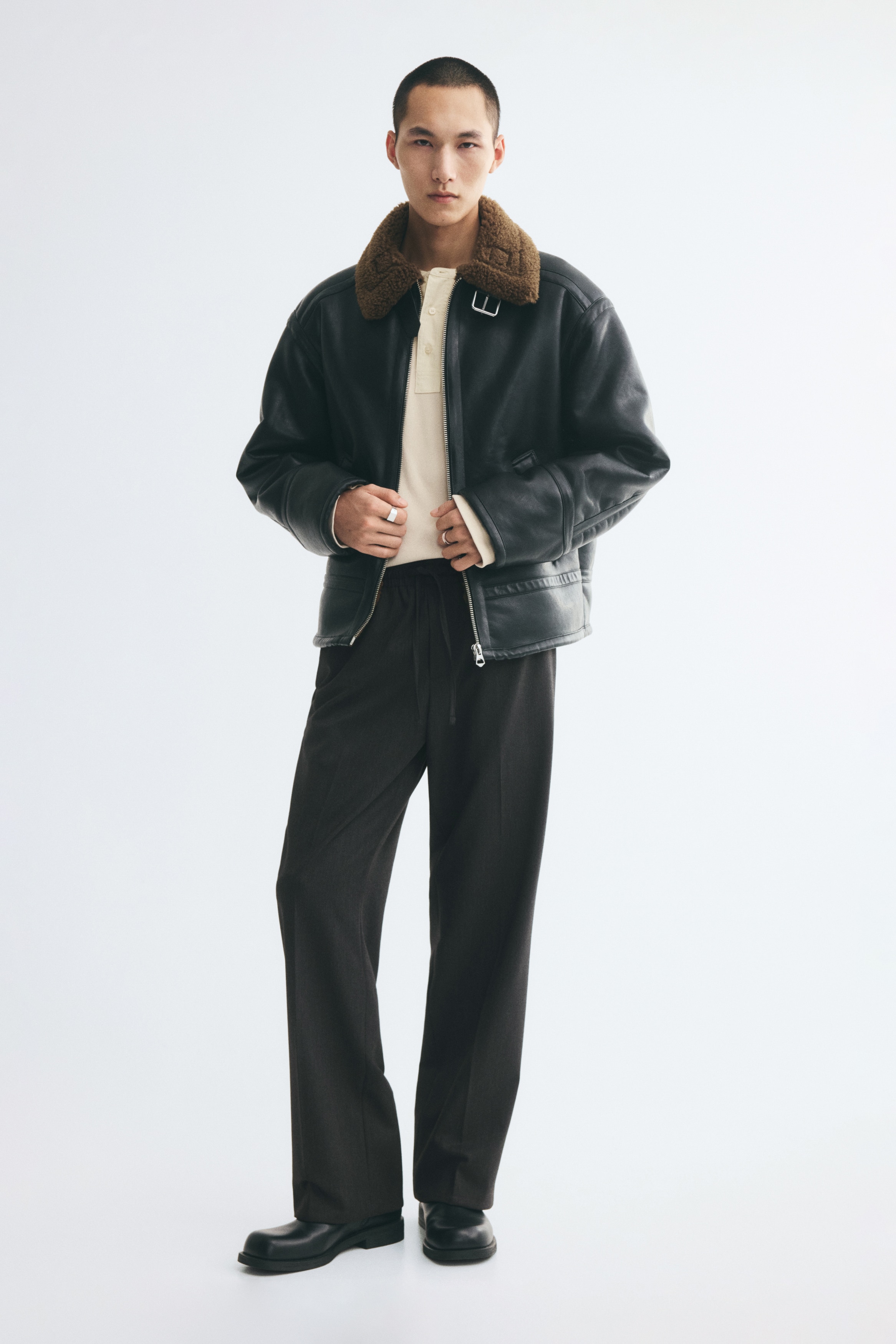 Dark grey trousers are shown from the front, featuring an elasticated waistband with matching drawstrings. The trousers display a straight-leg silhouette with sharp pressed creases running down the centre of each leg.