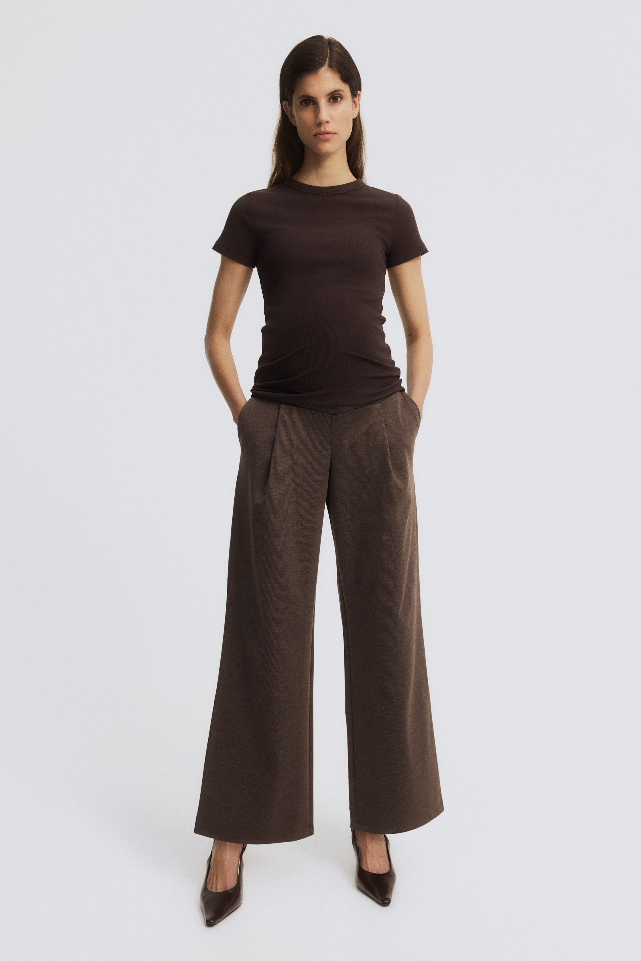 Zobacz większy obraz: Modelka ma na sobie luźne spodnie z ciężkiej, teksturowanej dzianiny, stojąc z rękami w ukośnych kieszeniach bocznych. Spodnie charakteryzują się szerokim panelem w pasie z miękkiej dzianiny oraz szerokimi nogawkami z zakładkami z przodu.