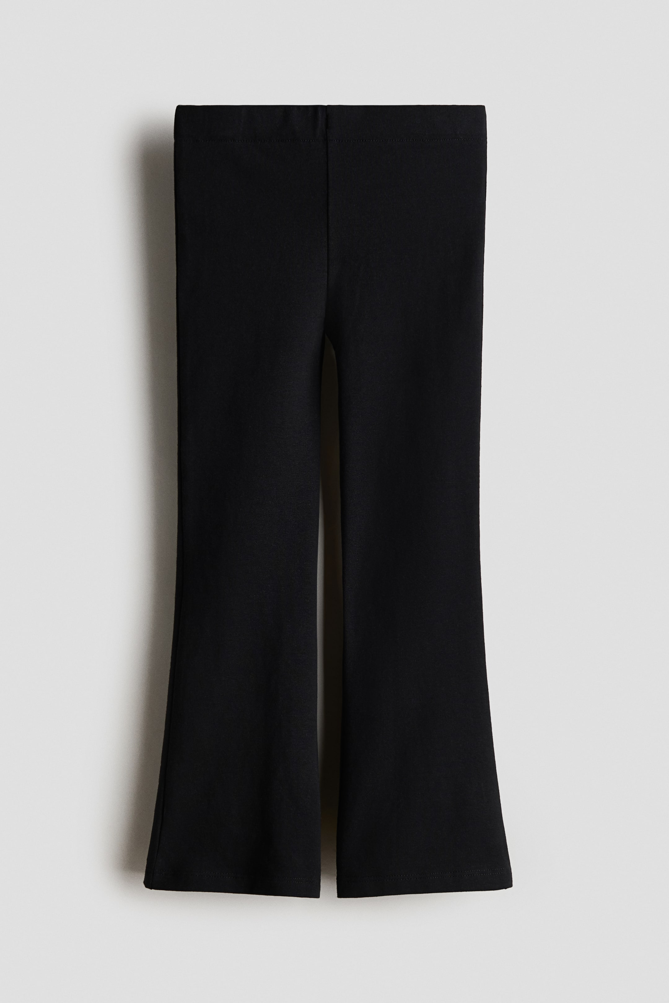 View larger image: Black flared trousers feature a flat waistband, with the legs fitting through the thigh and flaring from the knee to the hem.