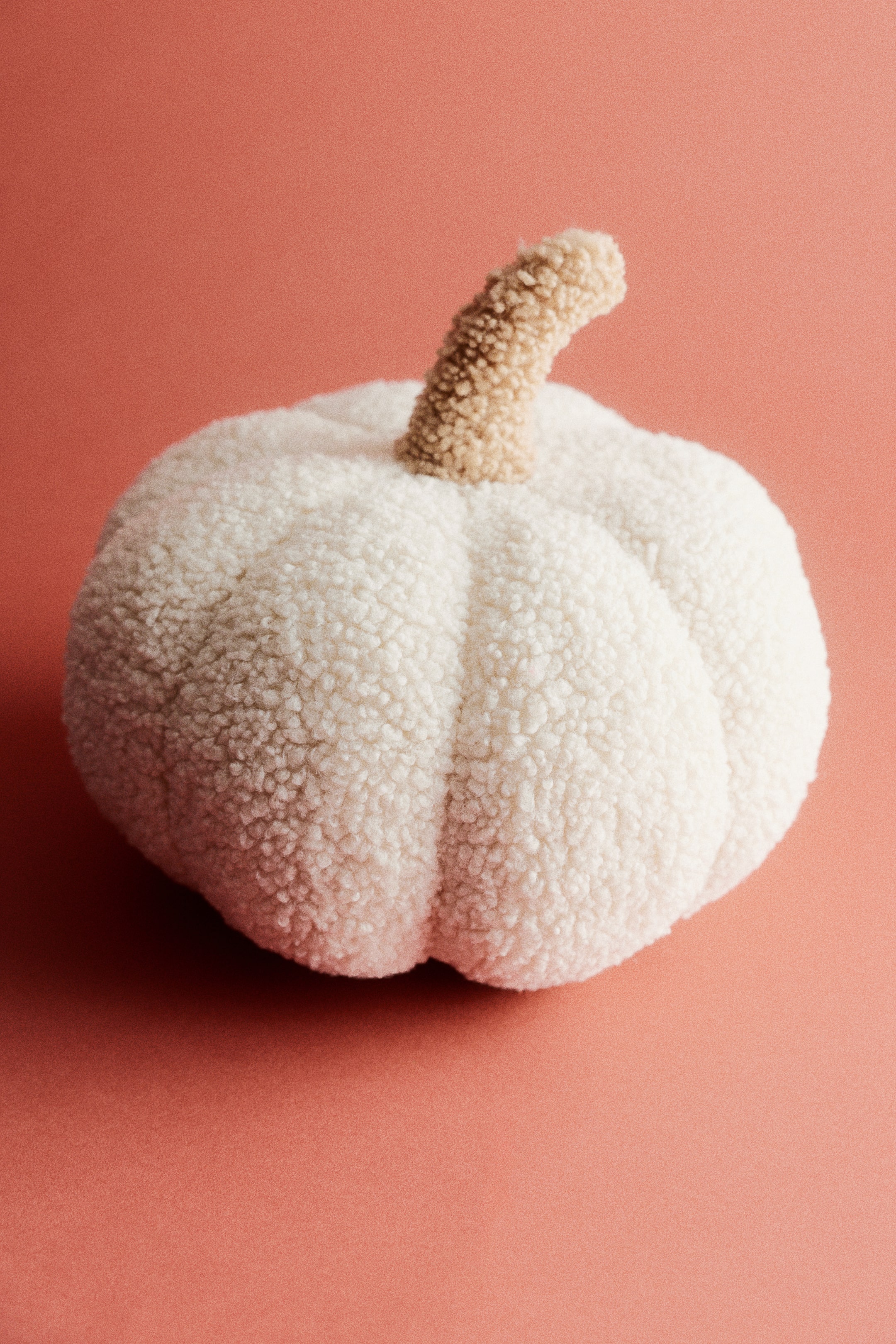 Visualizza l'immagine ingrandita: Un cuscino a forma di zucca mostra un morbido corpo in teddy fleece color crema-bianco, testurizzato e con segmenti verticali ben definiti. Il cuscino presenta nella parte superiore un gambo curvo, testurizzato, di colore beige chiaro.